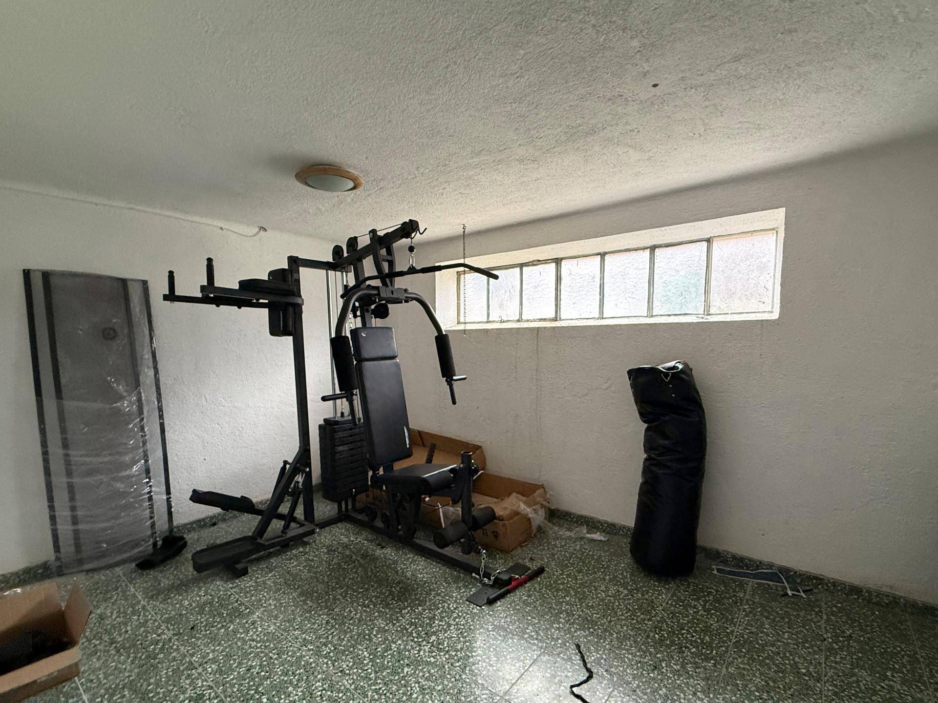 Fitnessraum im Keller mit Trainingsgerät, Boxsack und kleinem Fenster für Belüftung.