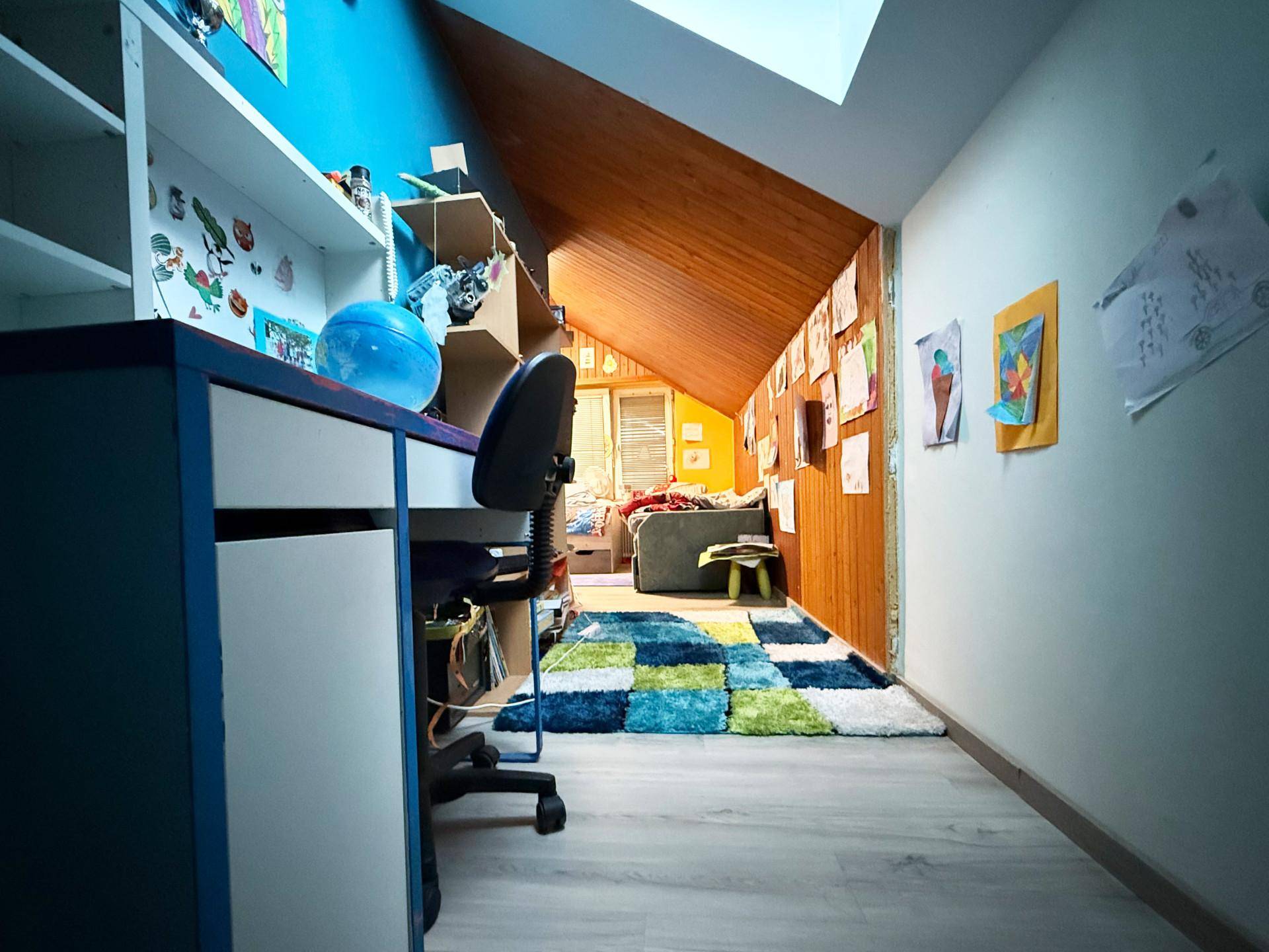 Dachgeschoss-Kinderzimmer mit Schreibtisch, farbenfrohem Teppich und einem Dachfenster.