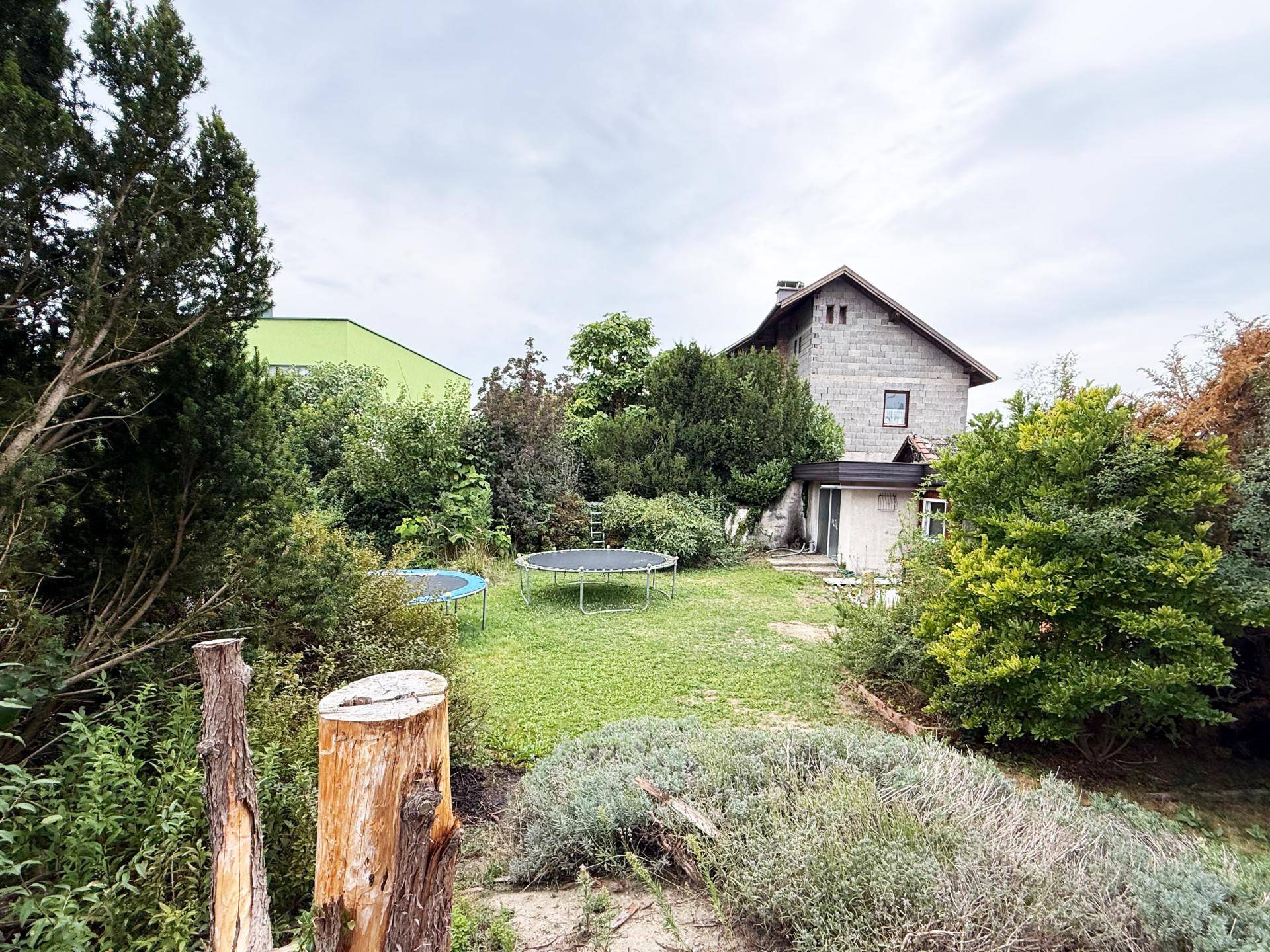 Großer Garten mit Rasenfläche, alten Bäumen und zwei Trampolinen, ideal für Familien.