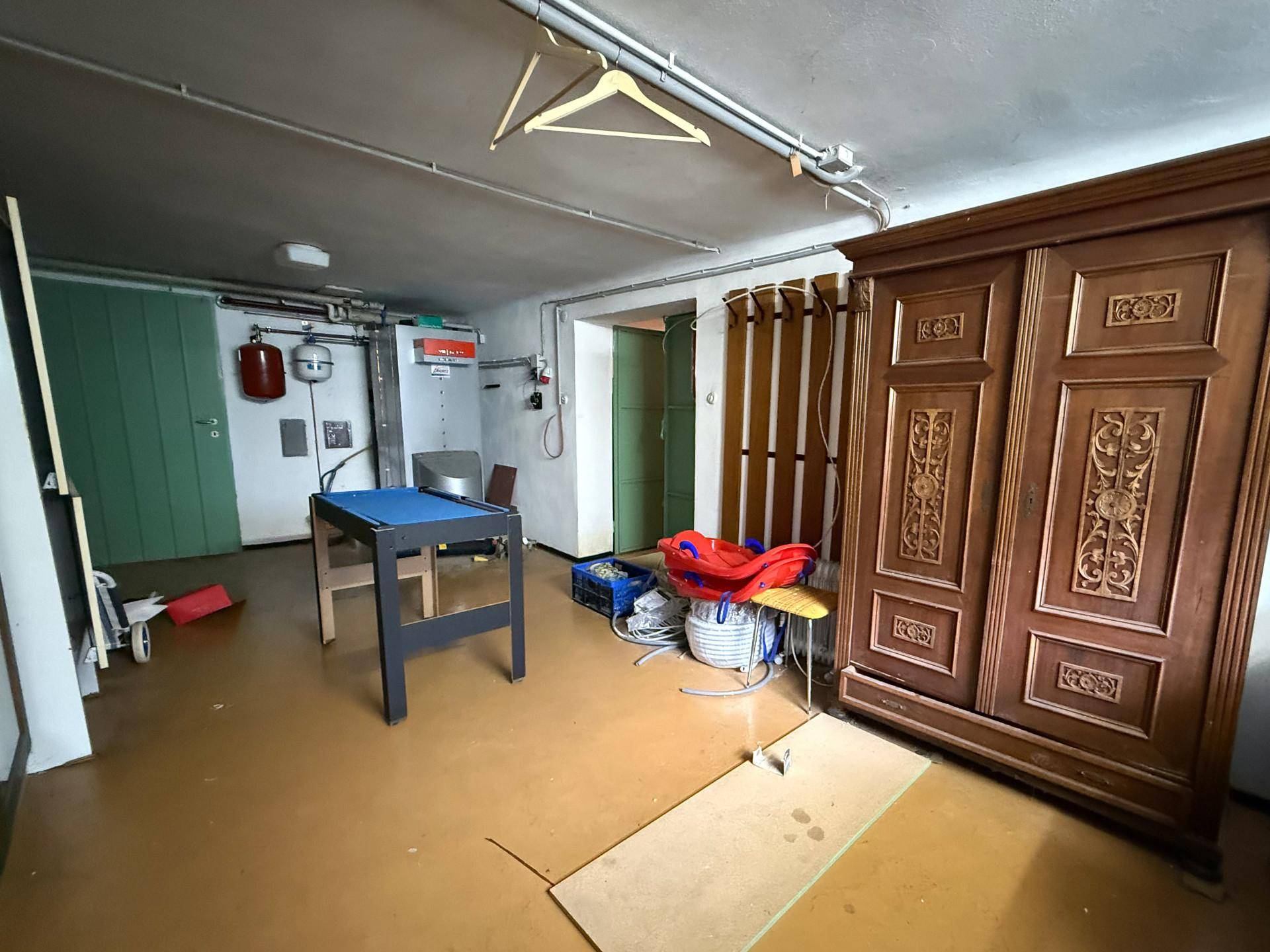 Kellerraum mit großem Holzschrank, kleinem Billardtisch und weiteren Lagergegenständen.