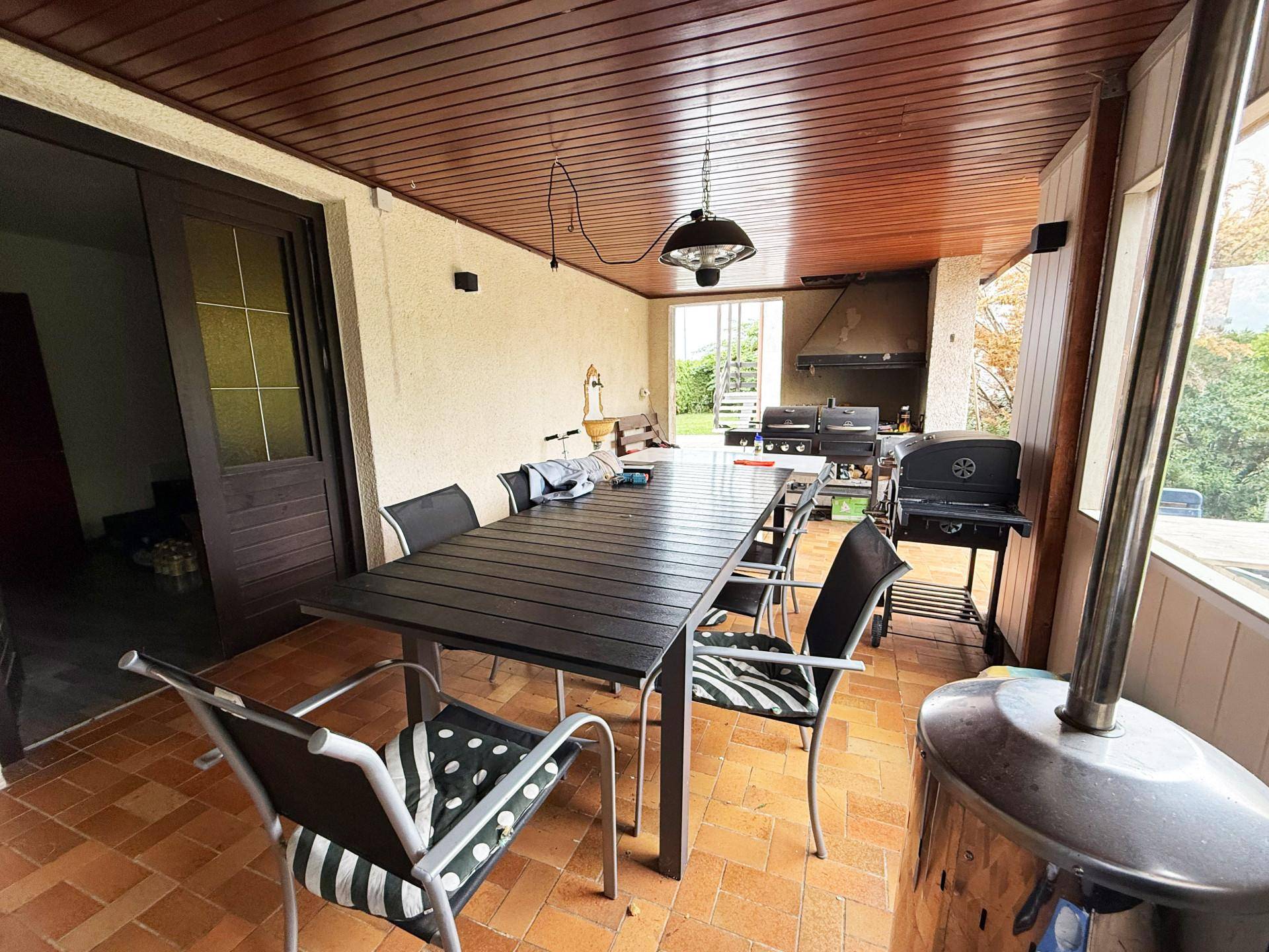 Überdachte Terrasse mit großem Esstisch, Stühlen und einem Grillbereich für gesellige Abende.