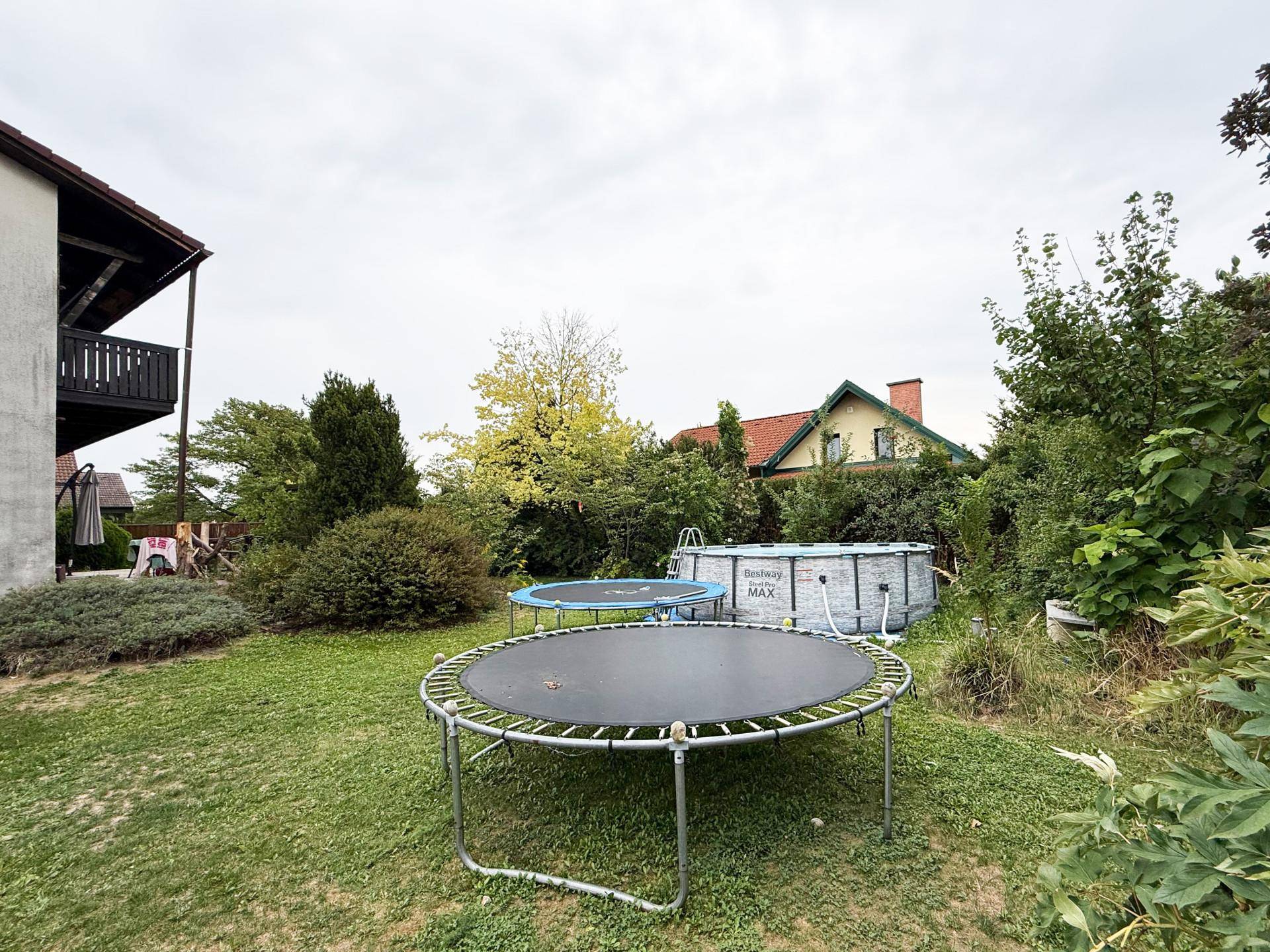 Gartenbereich mit Trampolin und einem Aufstellpool, umgeben von viel Grün.