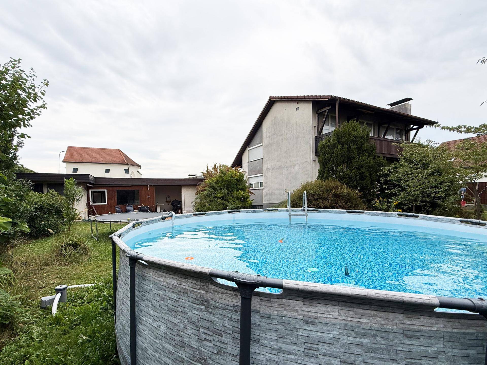 Garten mit großem Aufstellpool, umgeben von Bäumen und Sträuchern, ideal zur Abkühlung.