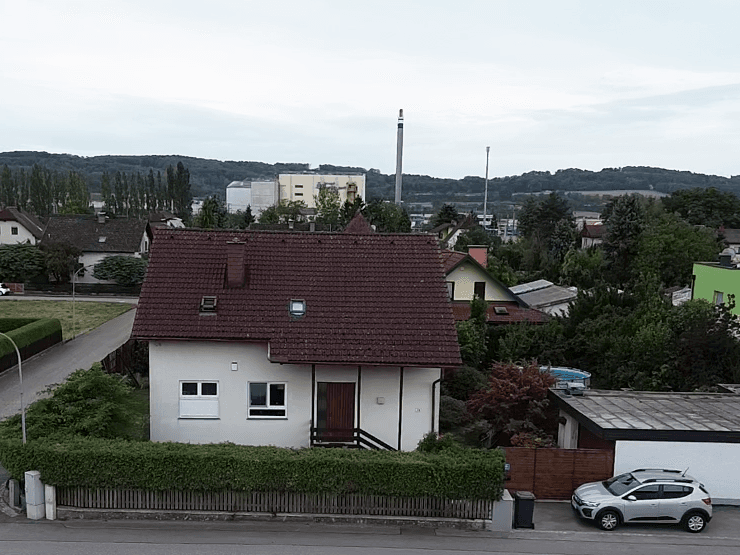 Luftaufnahme einer Wohnstraße mit Einfamilienhaus, viel Grün und Industrieanlagen im Hintergrund.