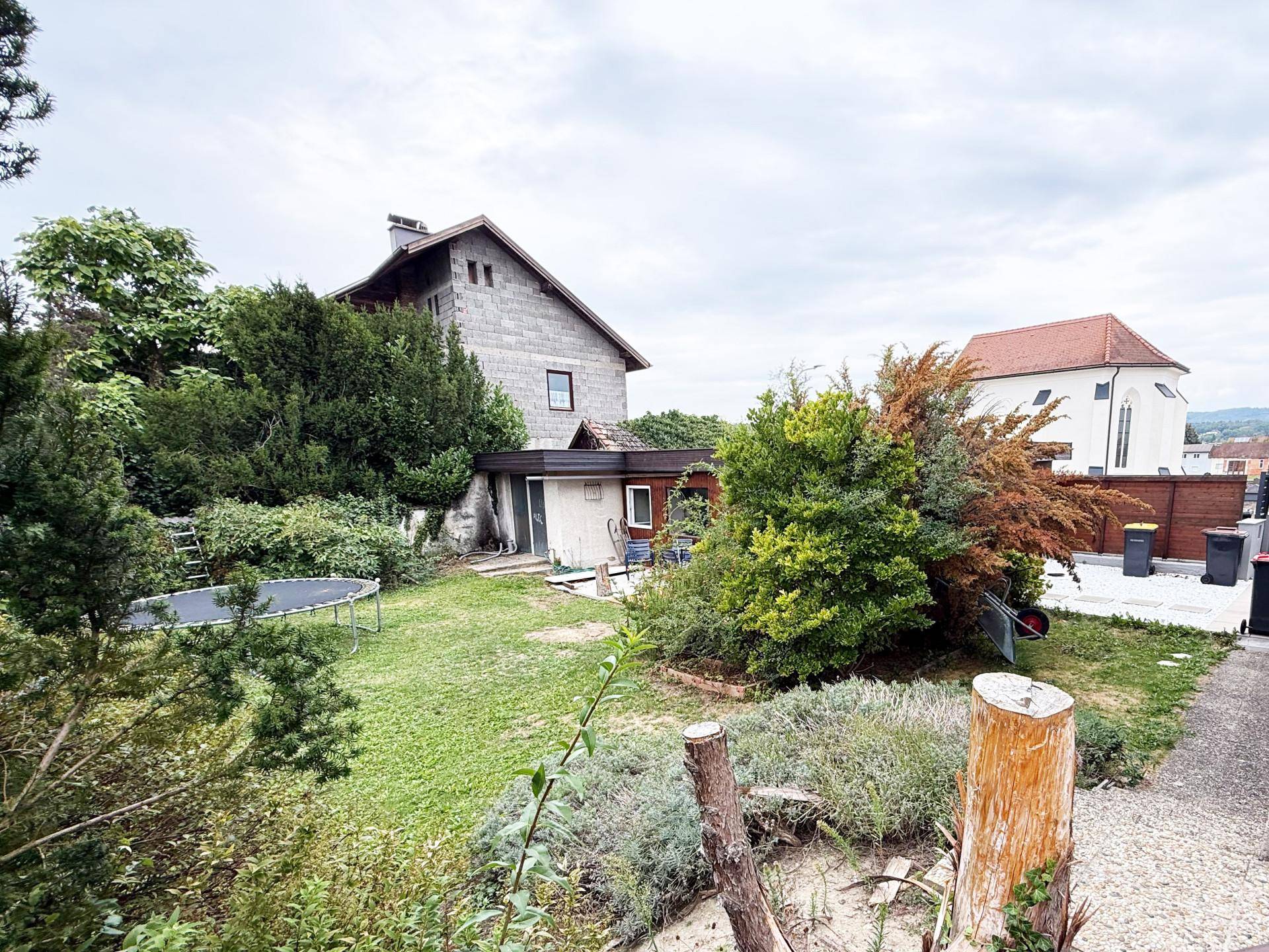 Blick auf den Garten mit Rasenfläche, Bäumen, Trampolin und dem Haus im Hintergrund.