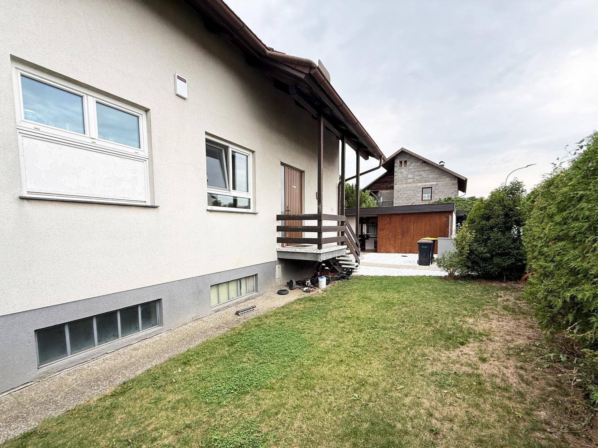 Seitenansicht des Hauses mit kleiner Rasenfläche und Kellerfenstern.