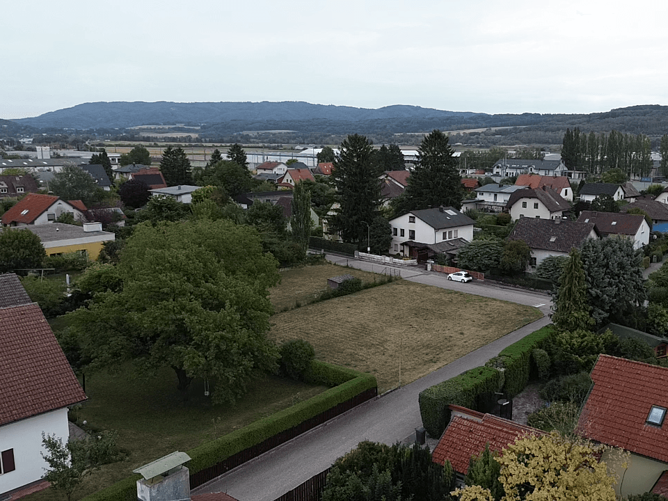 Weitläufige Luftaufnahme der Wohngegend mit Häusern, Grünflächen und fernen Hügeln.