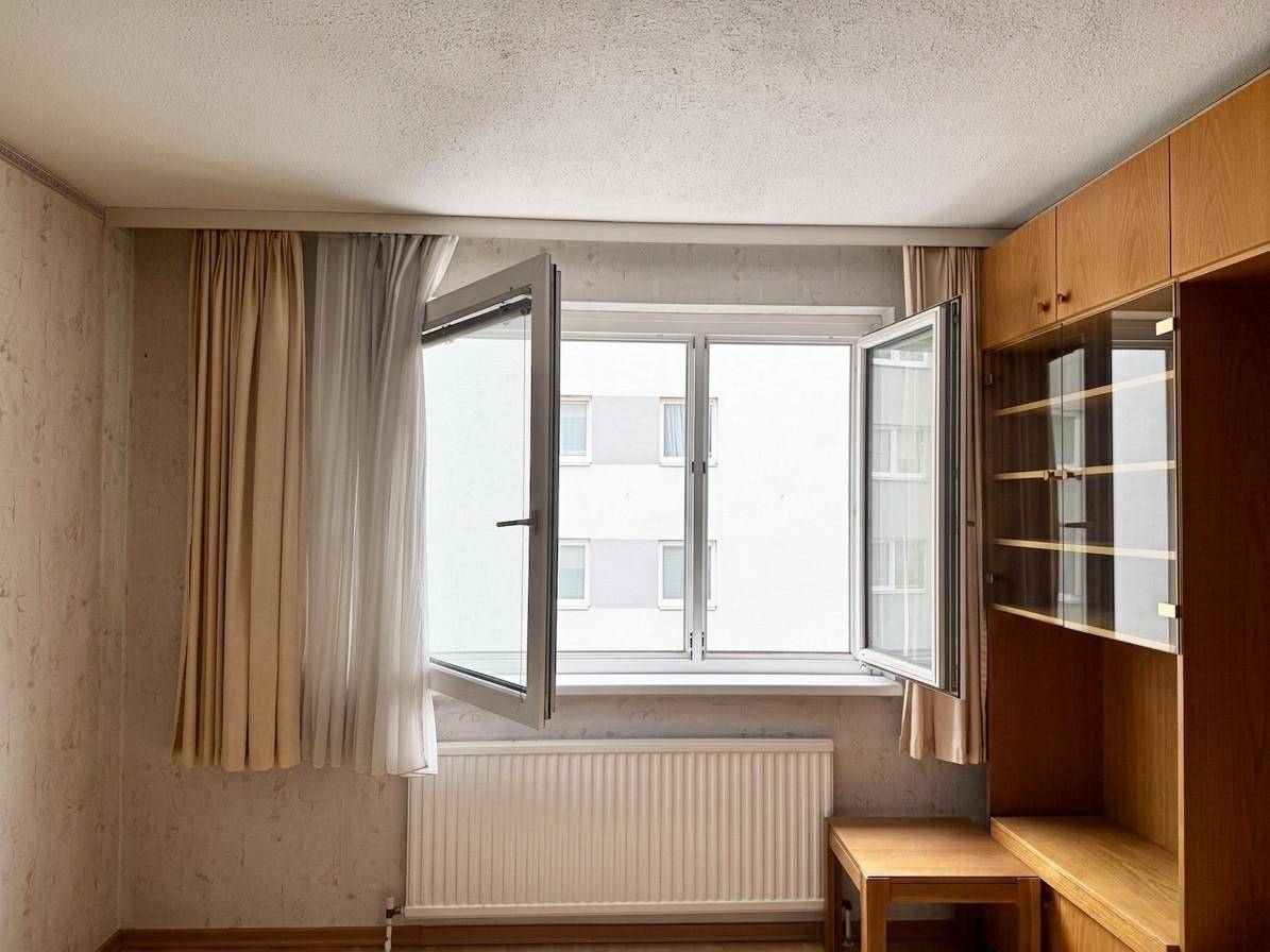 Heller Raum mit geöffnetem Fenster, Heizkörper und einem Holzschrank.