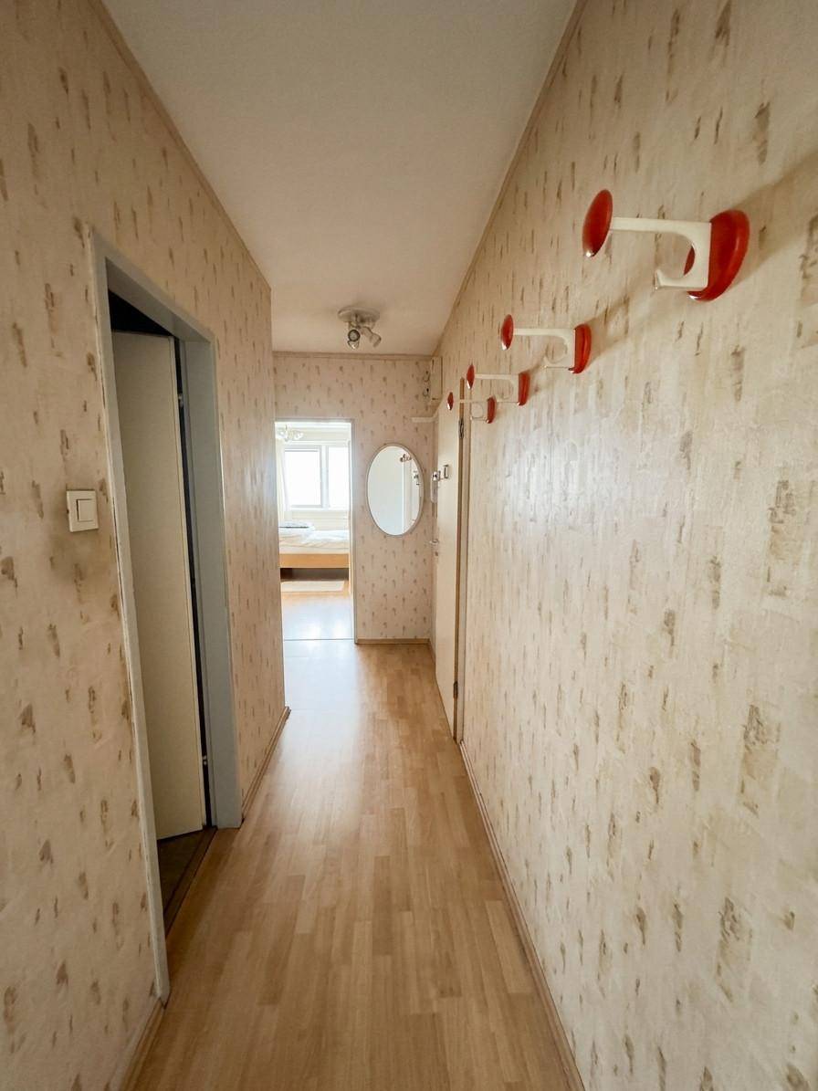 Langer Flur mit hellem Laminatboden, gemusterter Tapete und roten Garderobenhaken.