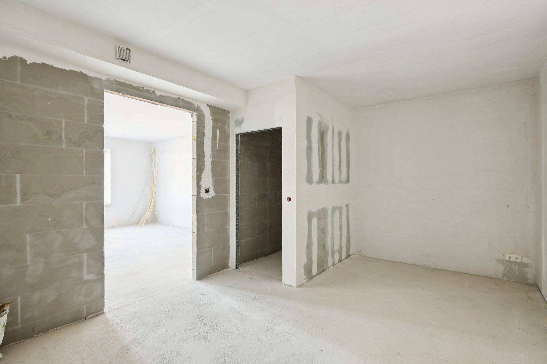 Unfertiger Innenraum im Rohbau mit unverputzten Wänden und sichtbaren Bauelementen.