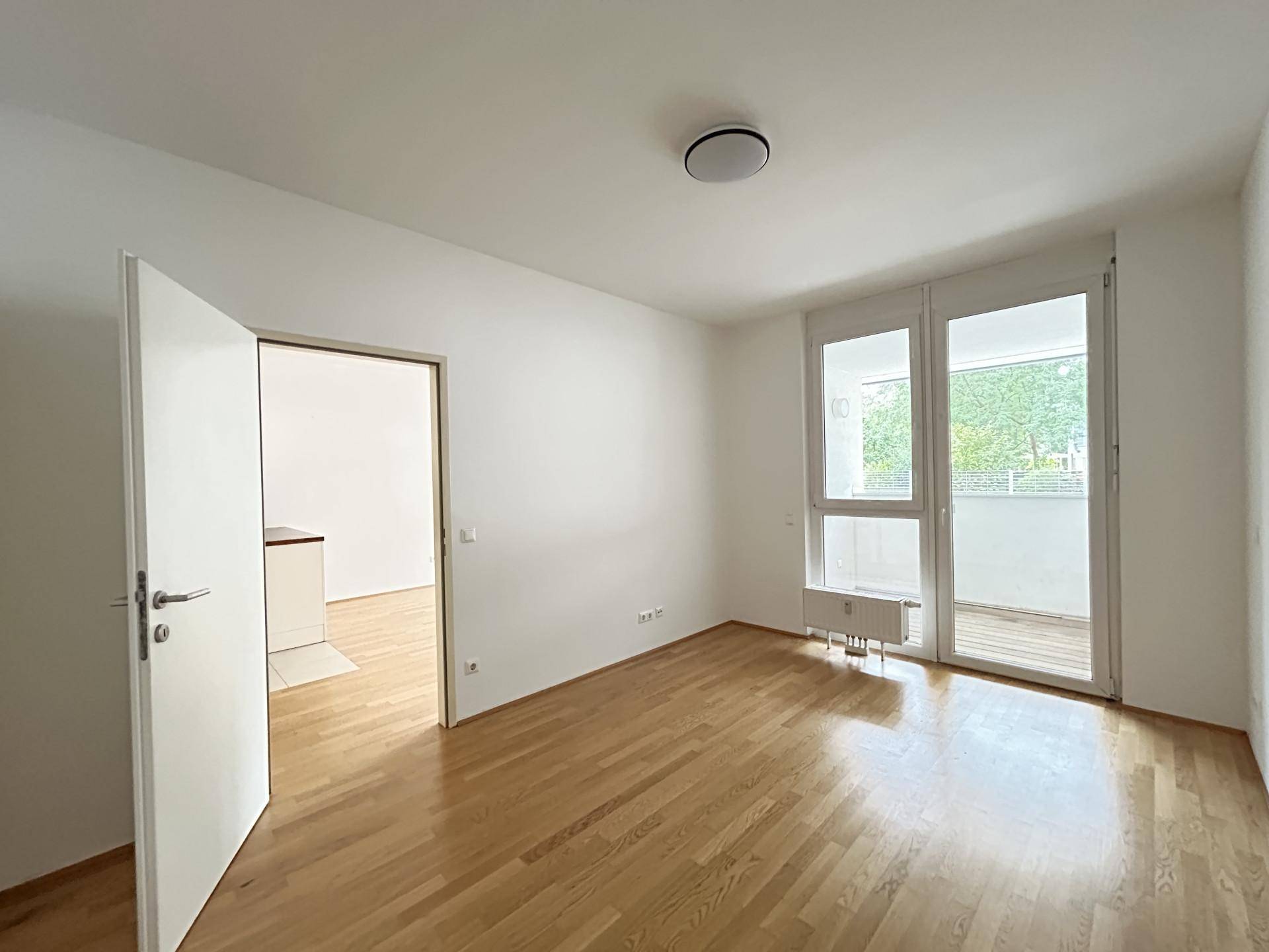 Heller Raum mit Holzboden und Zugang zu einem Balkon, der eine angenehme Wohnatmosphäre schafft.