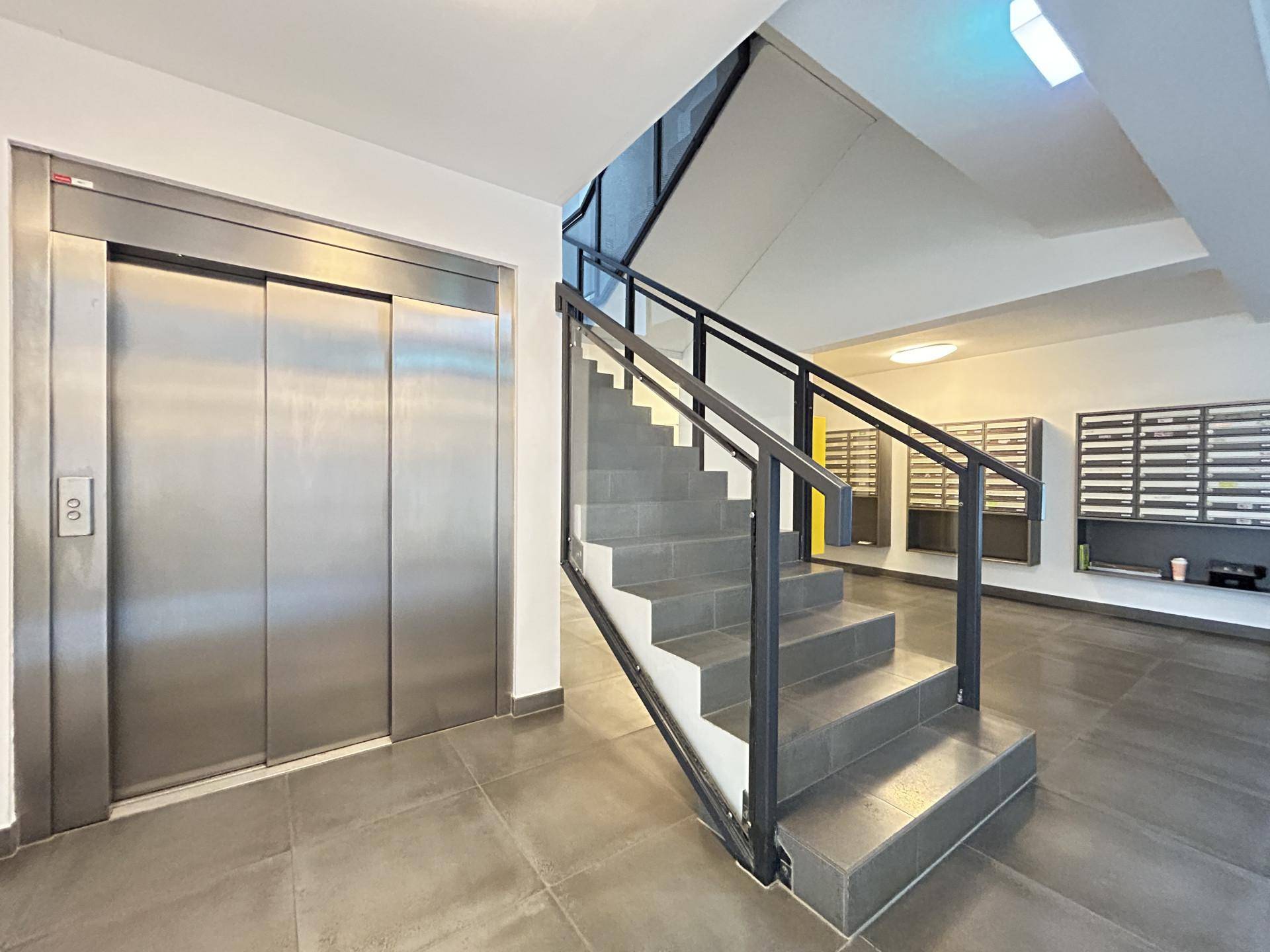 Moderner Eingangsbereich mit Aufzug, Treppe und Briefkästen, der einen einfachen Zugang bietet.