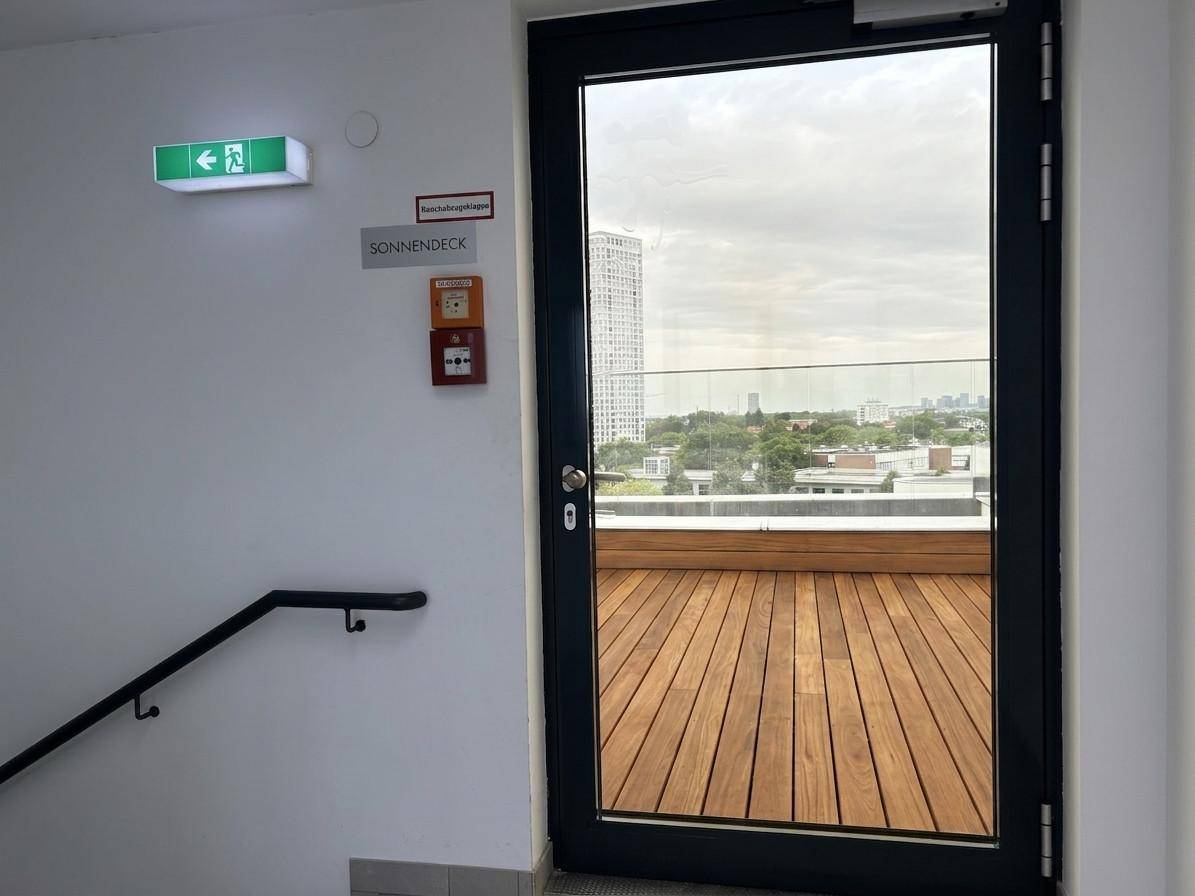 Zugang zu einer Dachterrasse mit Holzboden, die einen weiten Blick über die Stadt bietet.