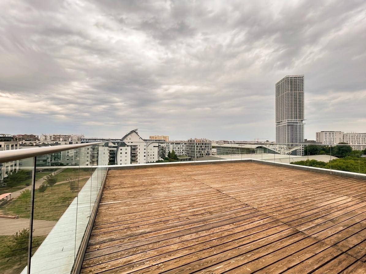 Weitläufige Dachterrasse mit Holzboden und Glasgeländer, ideal für Entspannung mit Stadtblick.