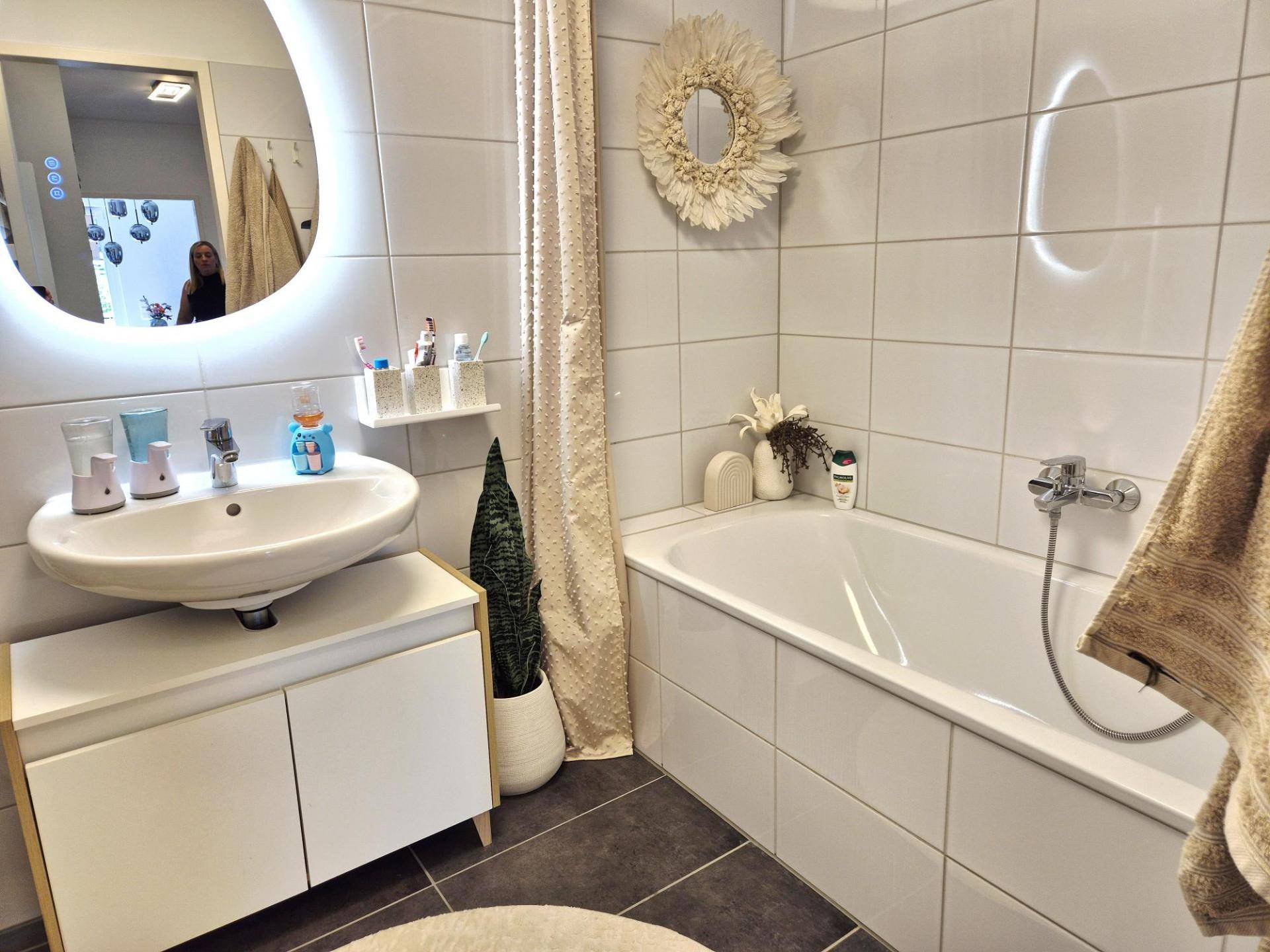 Modernes Badezimmer mit Badewanne, Waschtisch und beleuchtetem Spiegel.