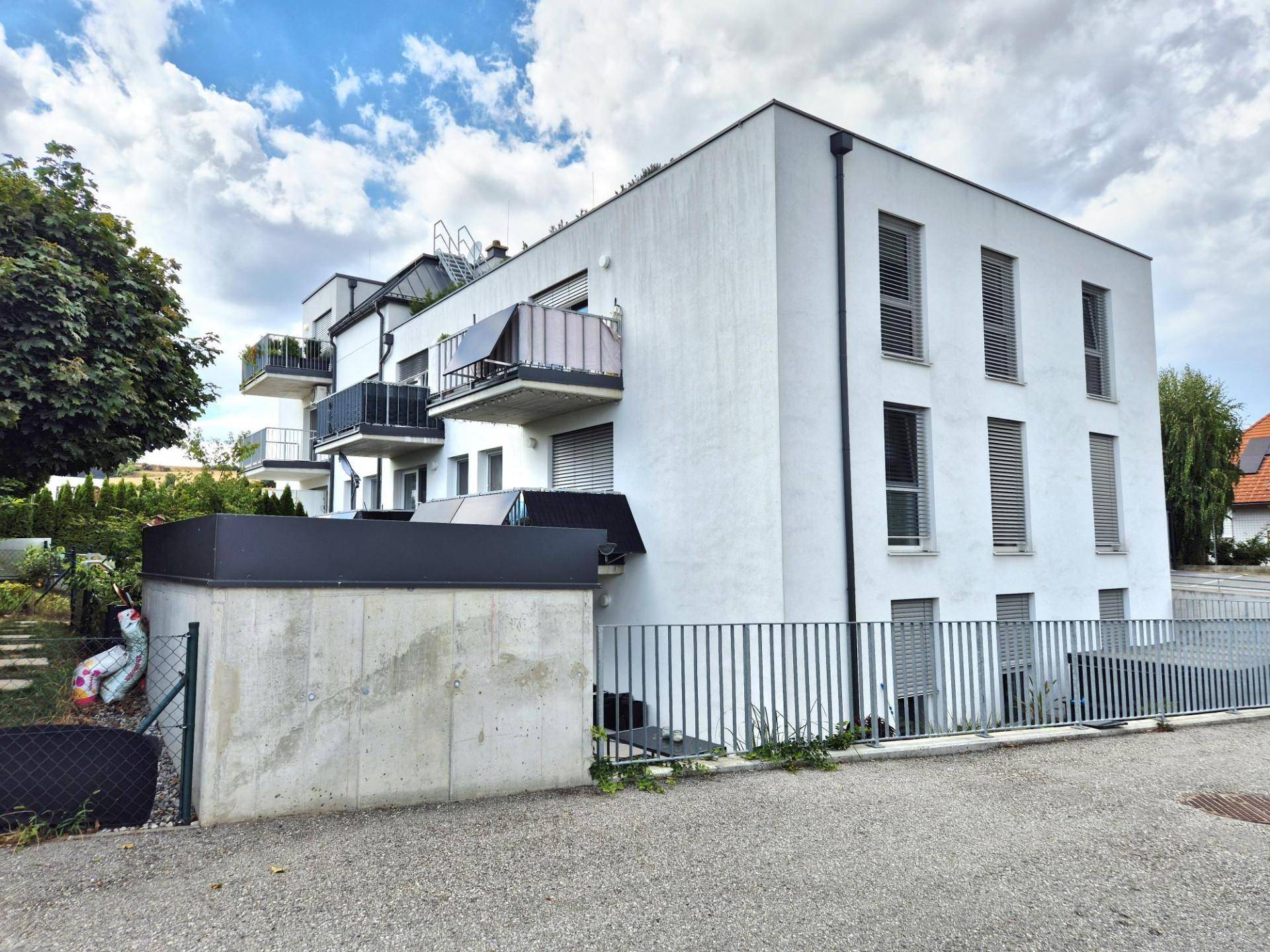 Neubau mit weißer Fassade, Balkonen und moderner Architektur in grüner Umgebung.