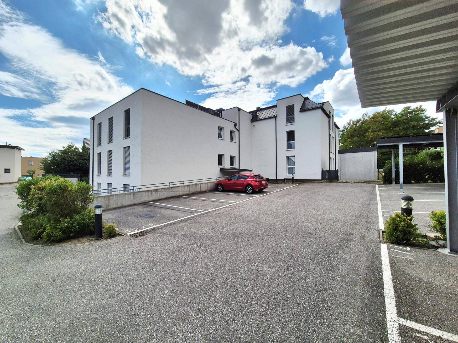 Moderne Wohnanlage mit weißer Fassade, Parkplätzen und barrierefreiem Zugang.