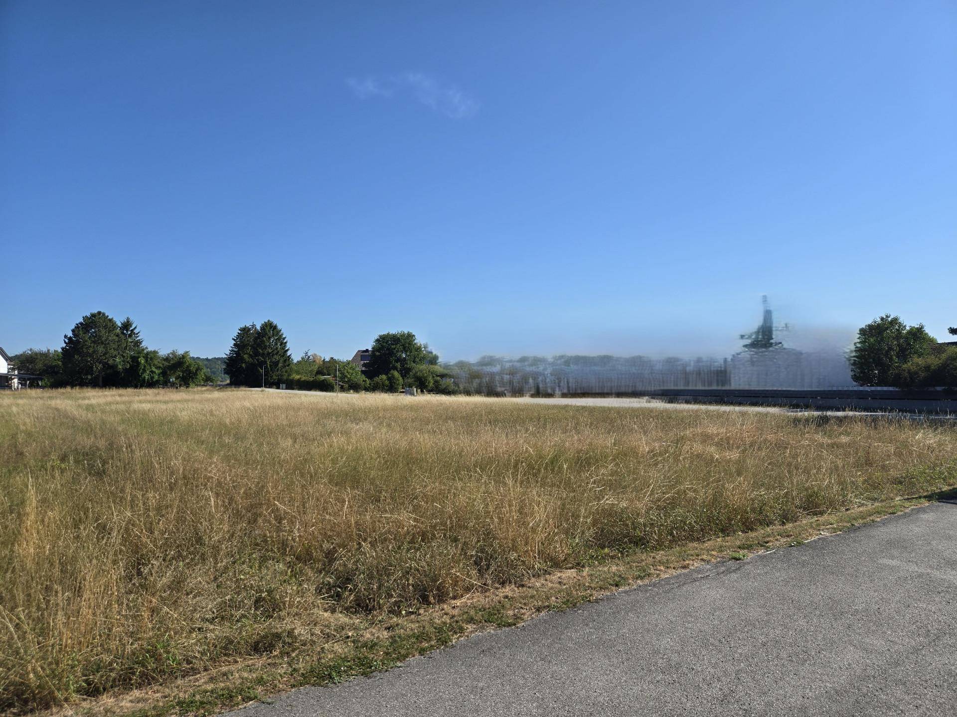 Ausgedehntes trockenes Feld mit einer unscharfen Gebäudestruktur in der Ferne unter strahlend blauem Himmel.