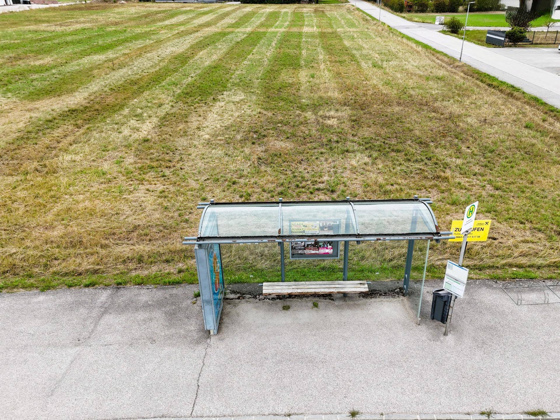 Luftaufnahme einer Bushaltestelle neben einem großen, gemähten Feld mit sichtbaren Mustern.