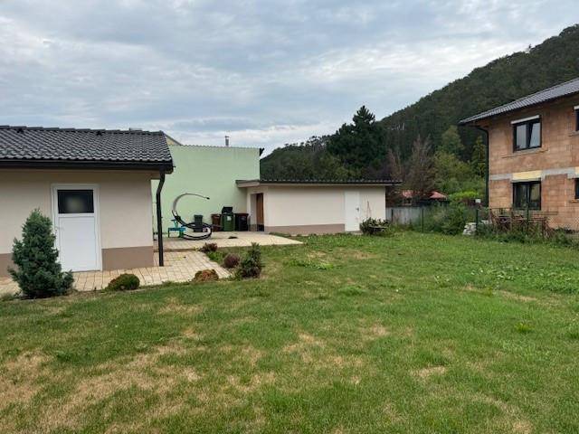 Großer, offener Gartenbereich mit Rasenfläche und Blick auf angrenzende Gebäude und bewaldete Hügel.