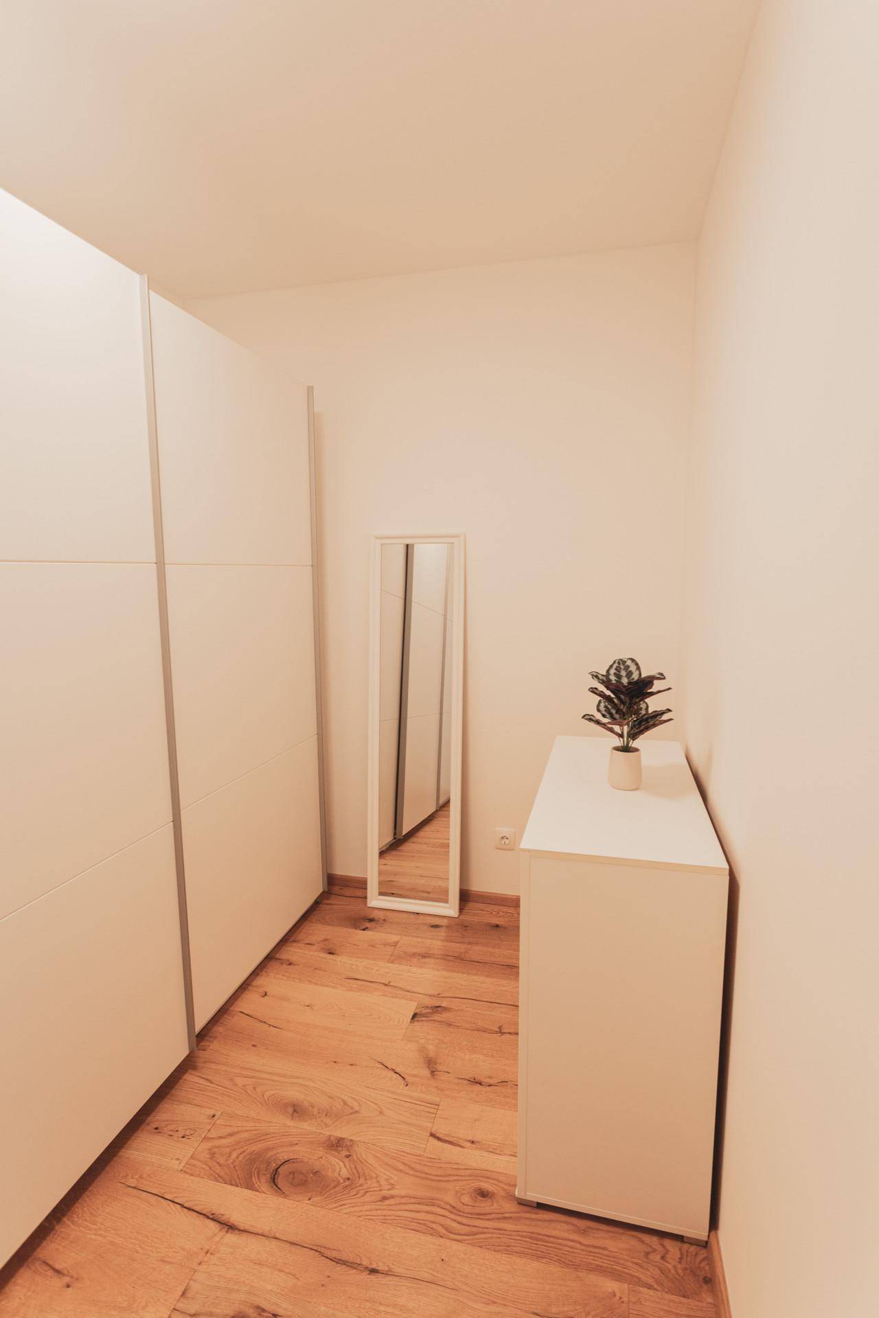 Heller Flur mit Einbauschränken, Holzboden und einem Ganzkörperspiegel.