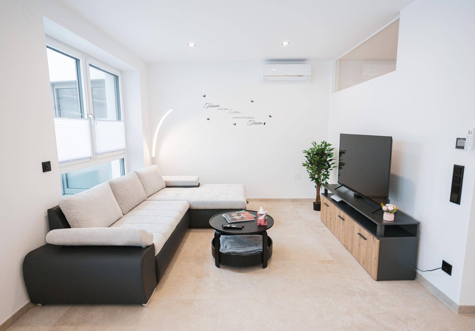 Gemütliches Wohnzimmer mit großem Ecksofa, Fernseher und Klimaanlage.