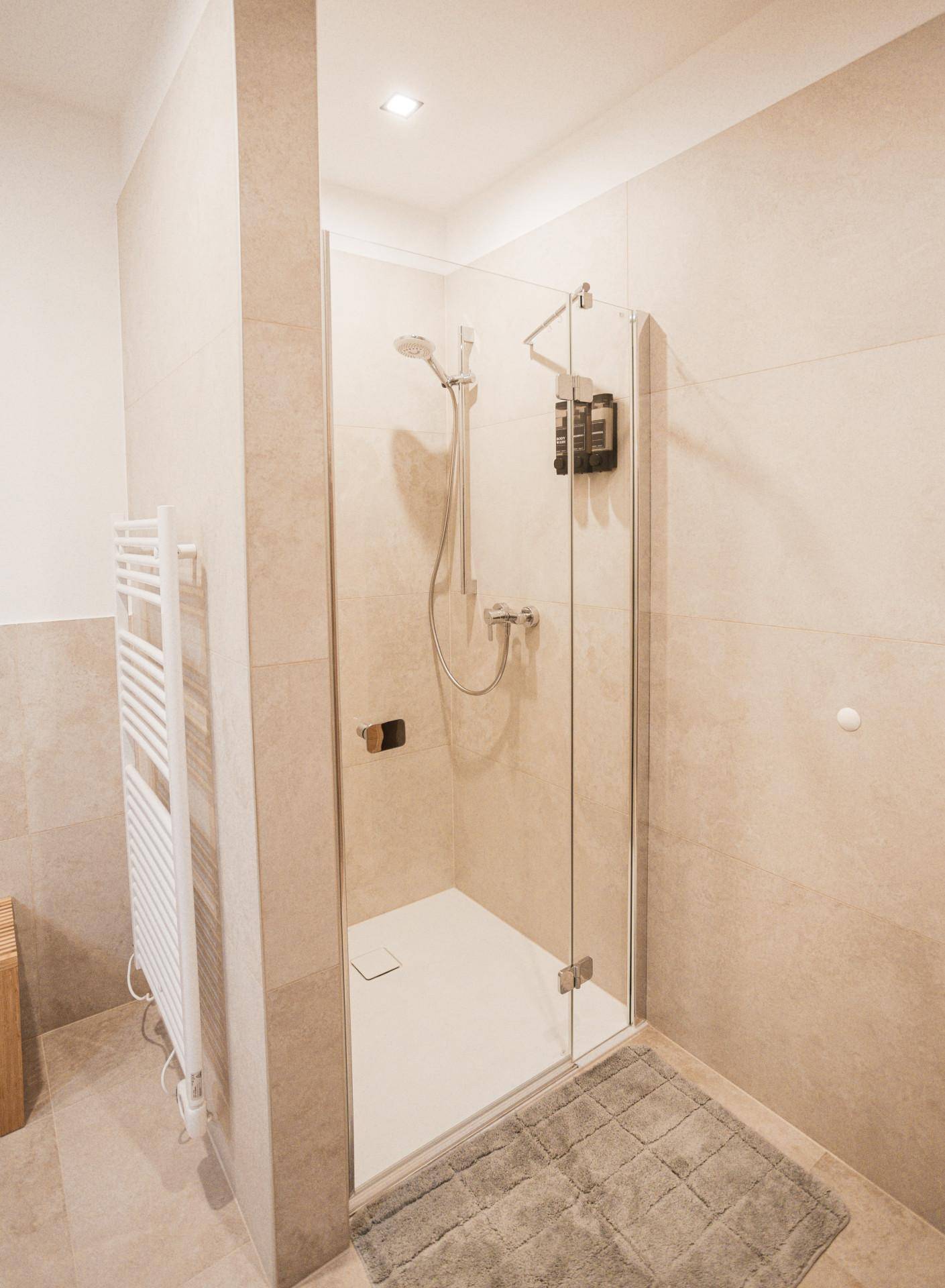 Moderne Duschkabine mit Glaswand und beigefarbenen Fliesen im Badezimmer.