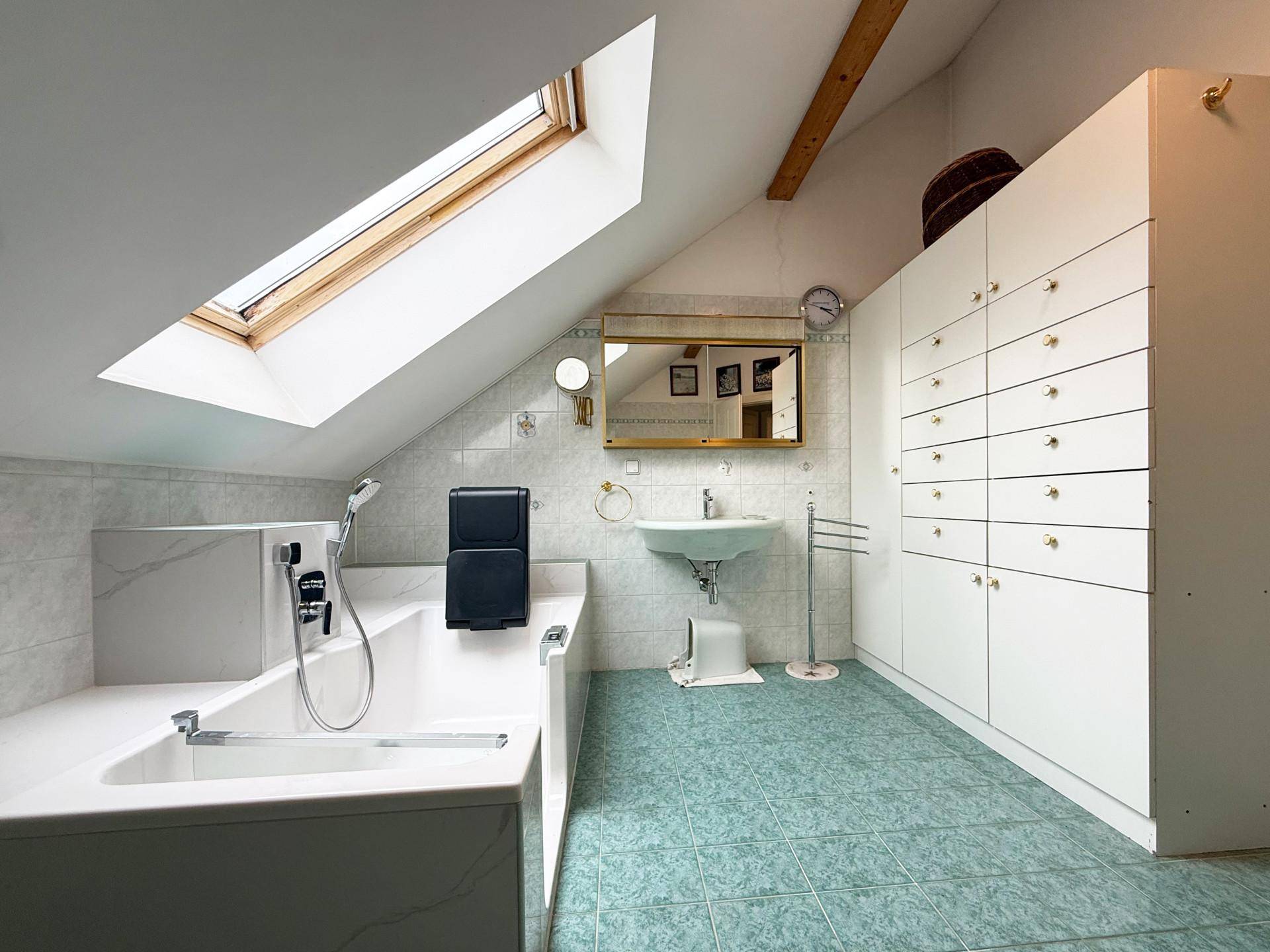 Helles Badezimmer im Dachgeschoss mit Badewanne, Dachfenster und praktischen Einbauschränken.