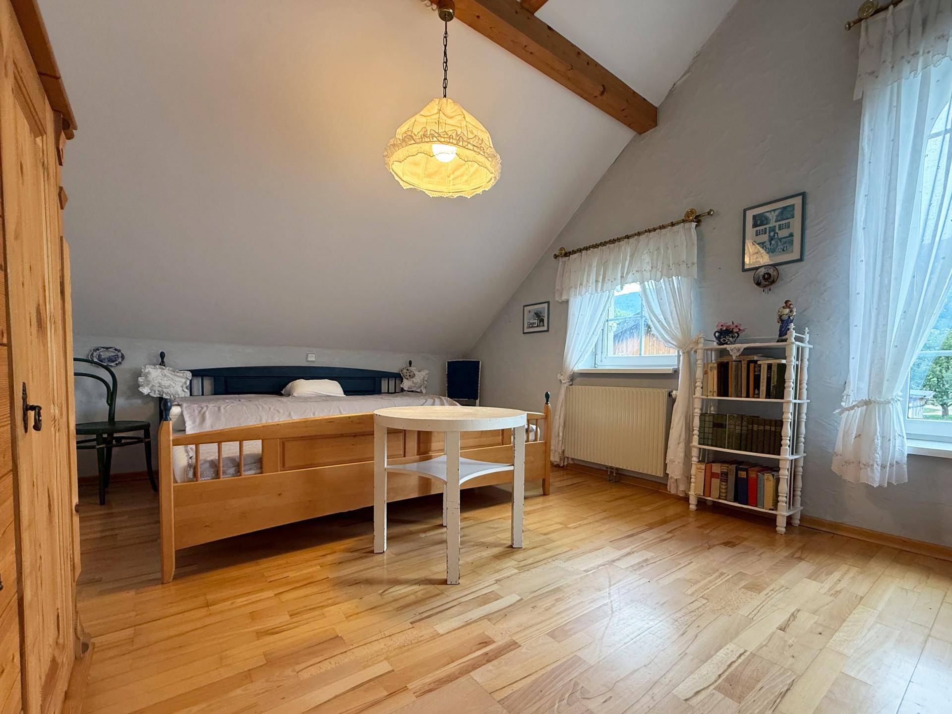Schlafzimmer im Dachgeschoss mit Holzboden, Dachschräge und traditionellen Vorhängen.