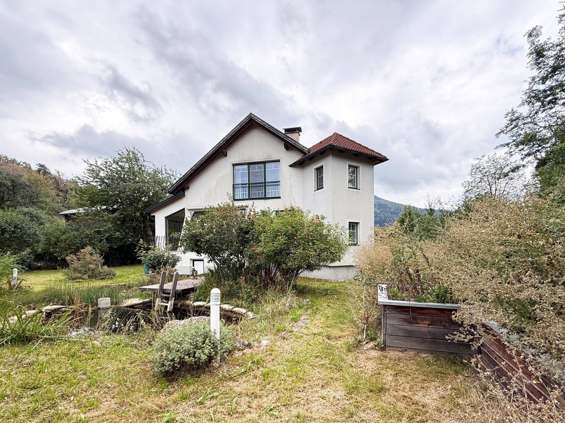 Das Haus ist von einem weitläufigen Garten mit Teich und üppiger Vegetation umgeben.