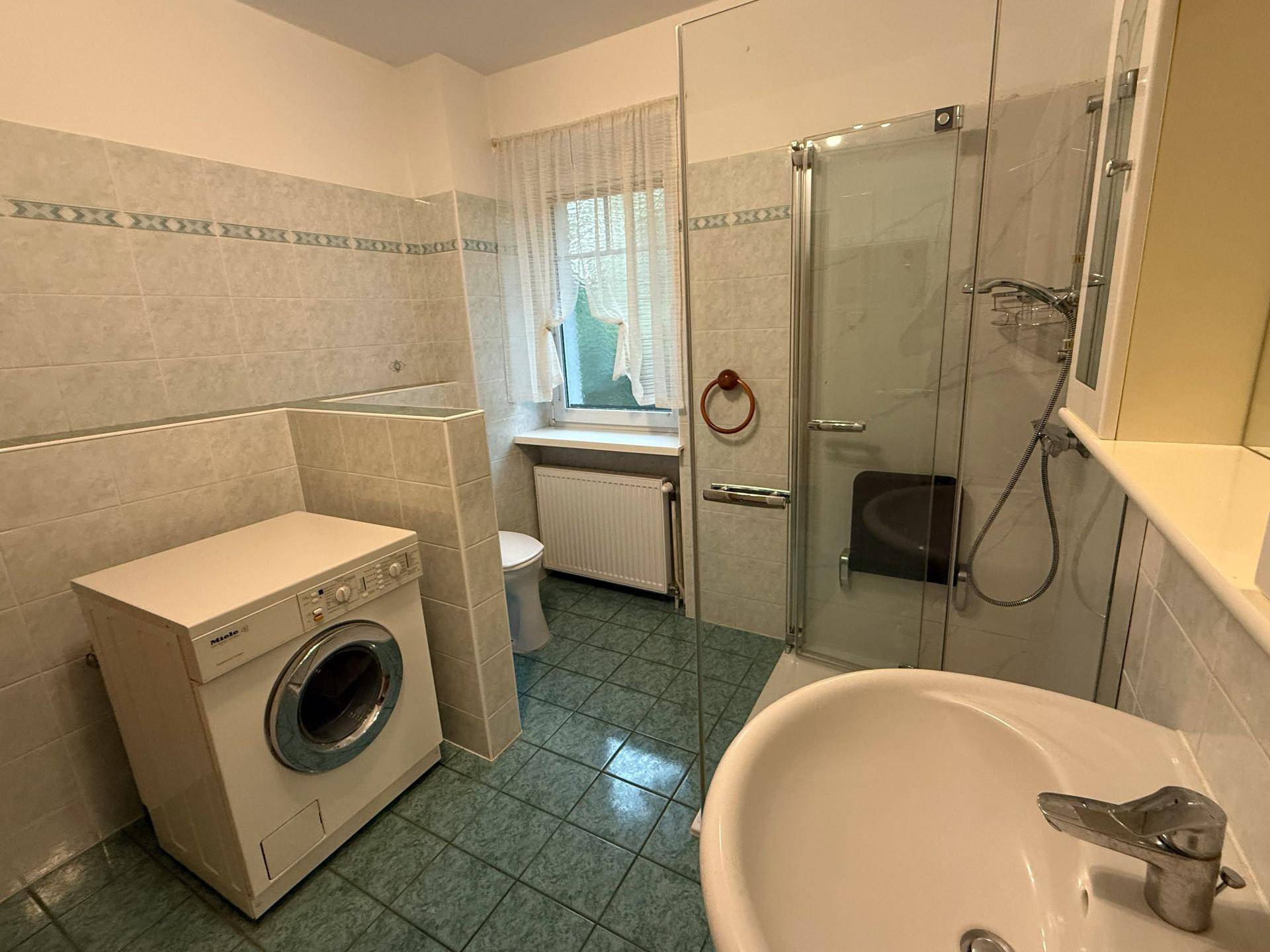 Badezimmer mit Duschkabine, Waschbecken, WC und Waschmaschine.