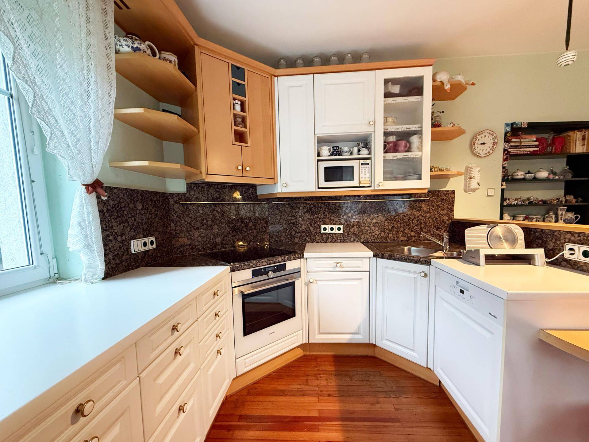 Traditionelle Küche mit Holzboden, weißen Schränken und dunkler Arbeitsplatte.