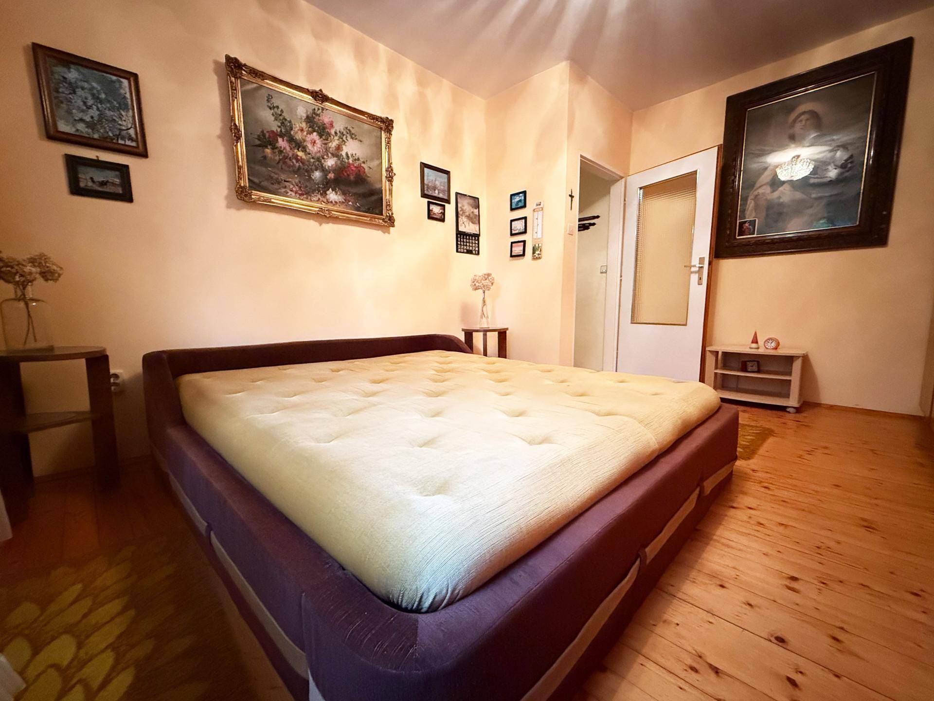 Schlafzimmer mit großem Bett, Holzboden und traditionellen Bildern an der Wand.
