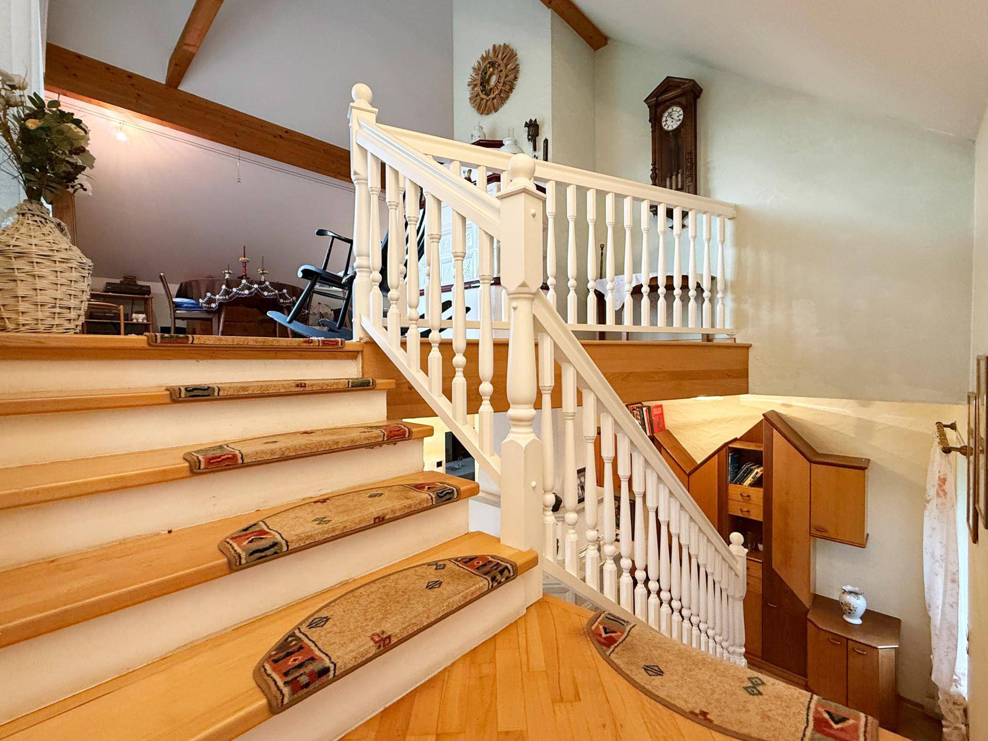 Holztreppe mit weißem Geländer, die zum Wohnbereich im Dachgeschoss führt.