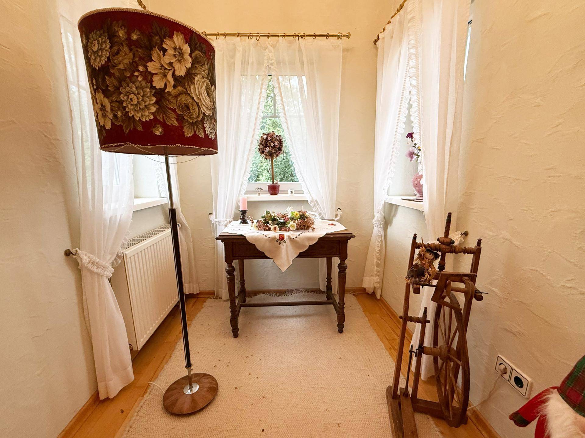 Kleiner Raum mit zwei Fenstern, Holztisch und traditioneller Stehlampe.