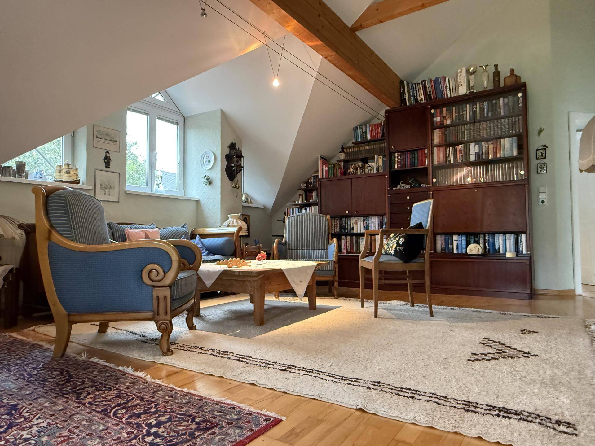 Gemütliches Wohnzimmer im Dachgeschoss mit Holzbalken, großem Bücherregal und traditionellen Möbeln.