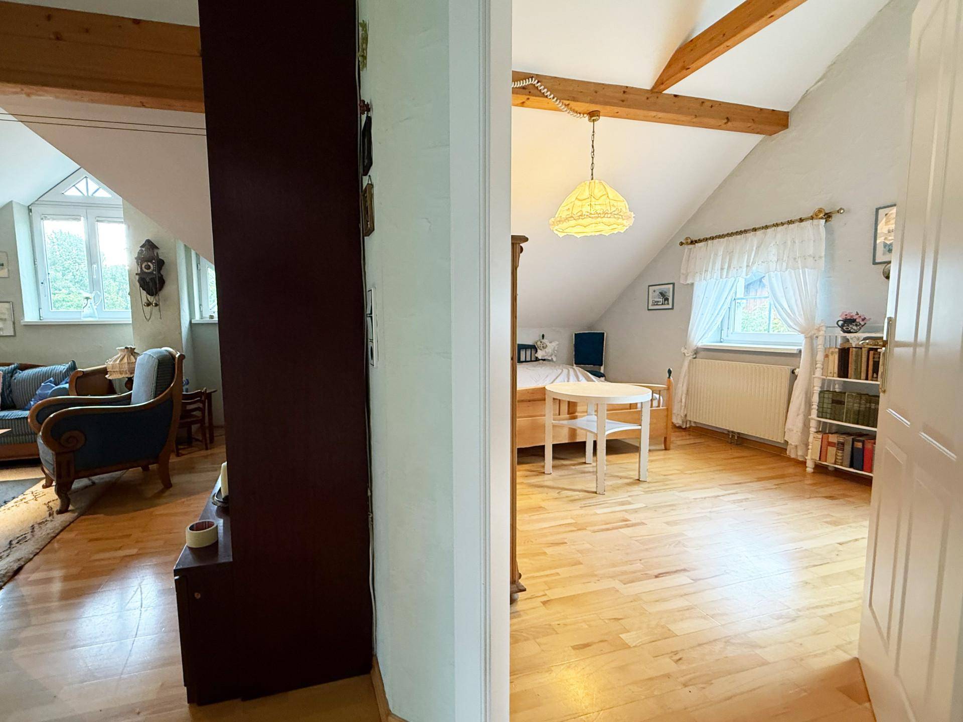 Flur mit Holztreppe und Blick in ein Schlafzimmer im Dachgeschoss mit schrägen Decken.