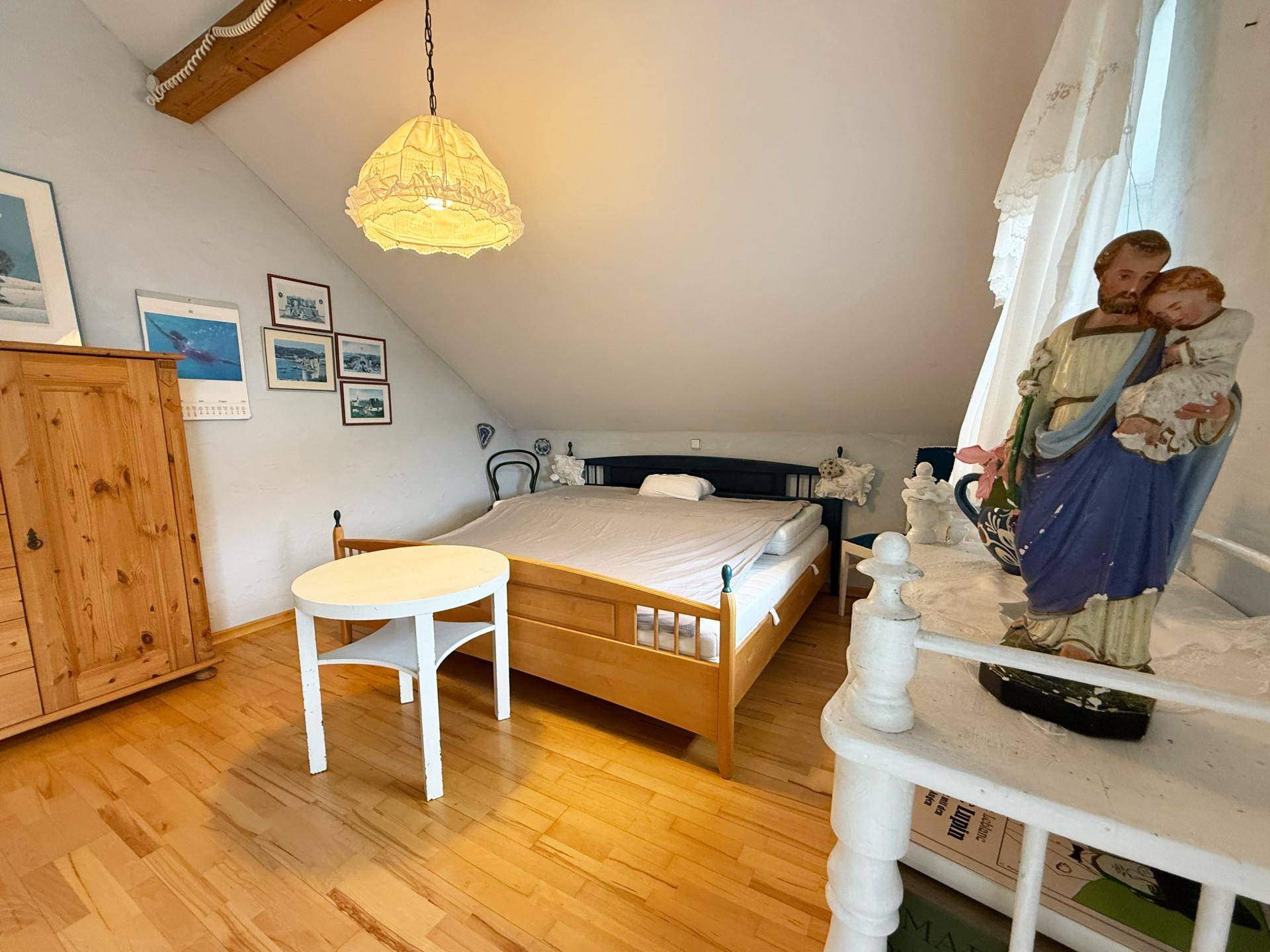 Schlafzimmer im Dachgeschoss mit Holzbalken, schrägen Decken und traditionellen Holzmöbeln.