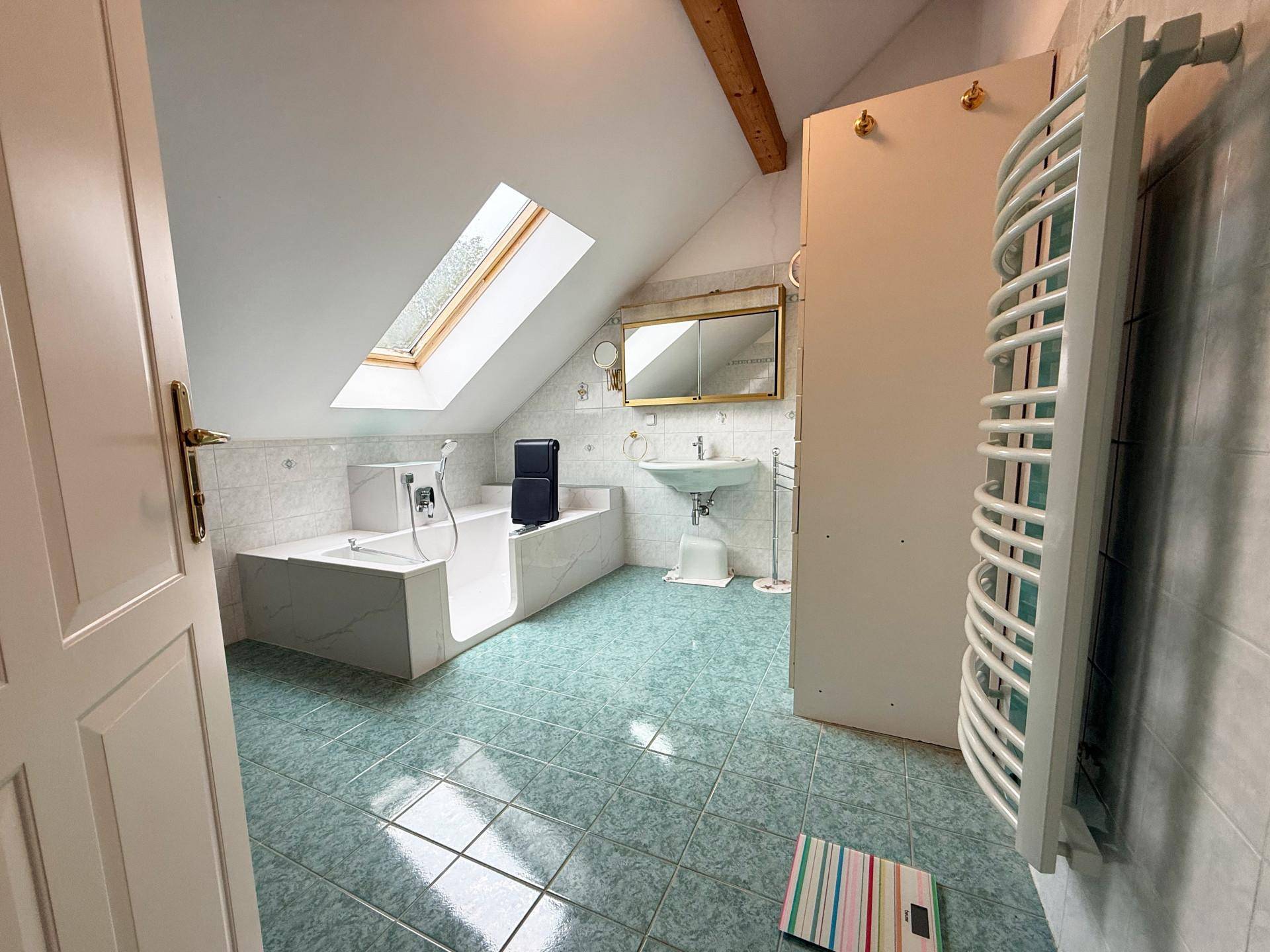 Badezimmer im Dachgeschoss mit Badewanne, grün gefliestem Boden und einem Dachfenster.