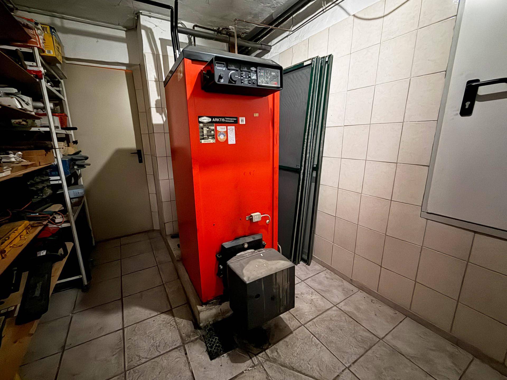 Heizungsraum im Keller mit einem großen roten Heizkessel und gefliesten Wänden.
