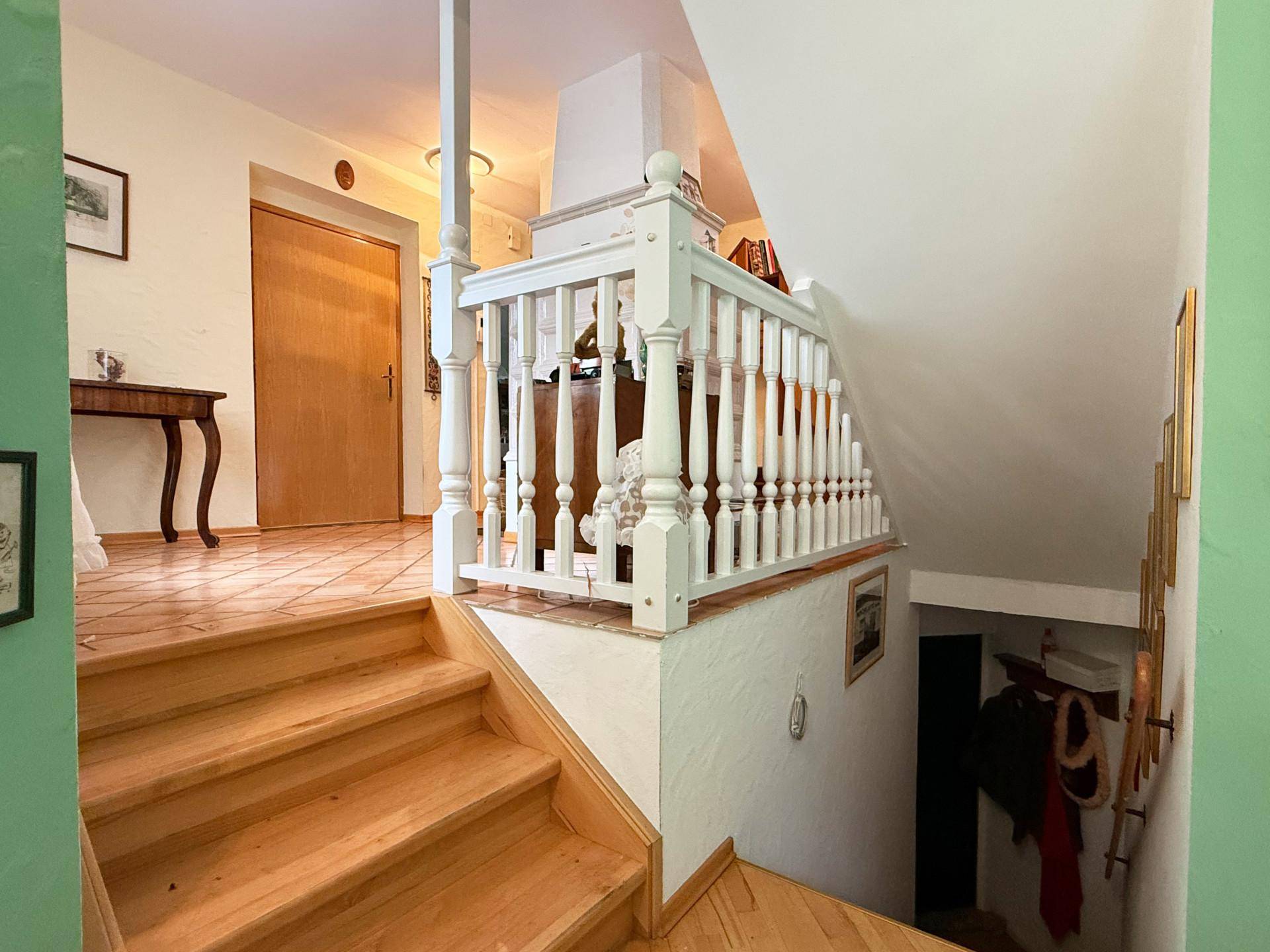 Heller Eingangsbereich mit Holztreppe und weißem Geländer, der zu den oberen Etagen führt.