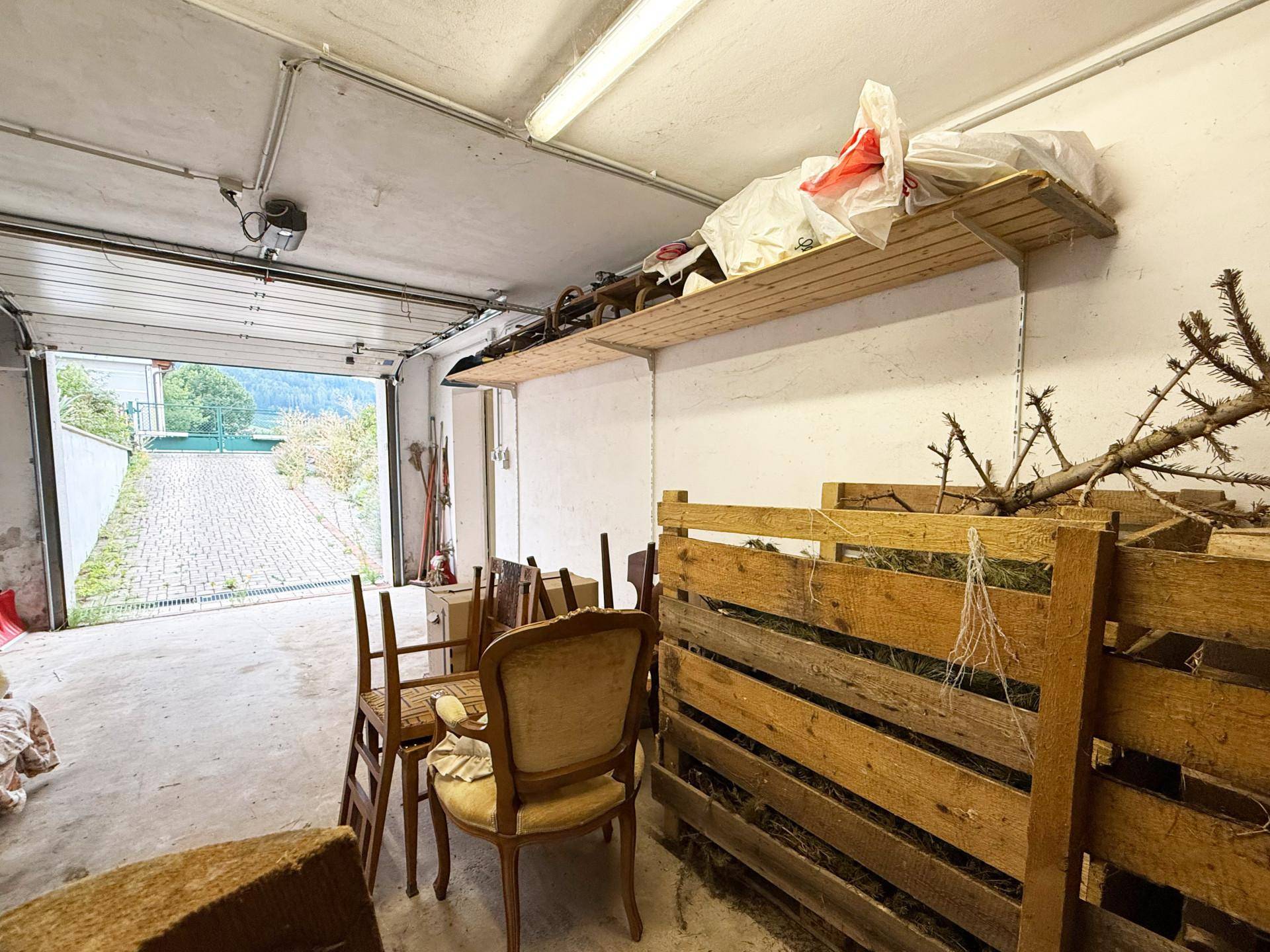 Garage mit offenem Tor, das auf eine gepflasterte Auffahrt führt, und Stauraum.
