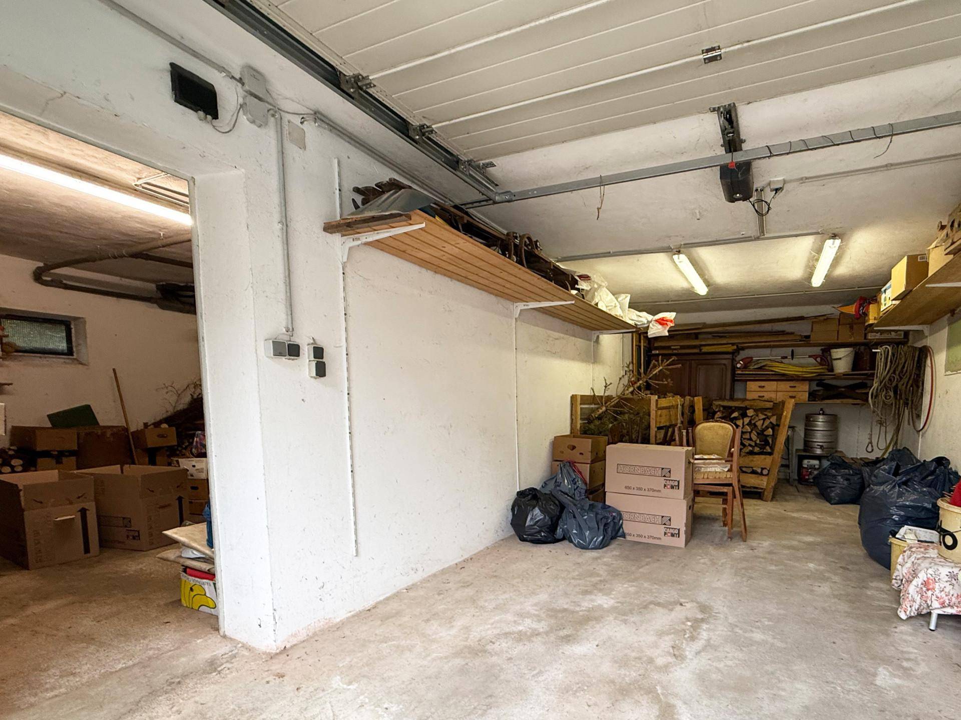 Geräumige Garage mit Betonboden, Regalen und viel Platz für Lagerung und Fahrzeuge.