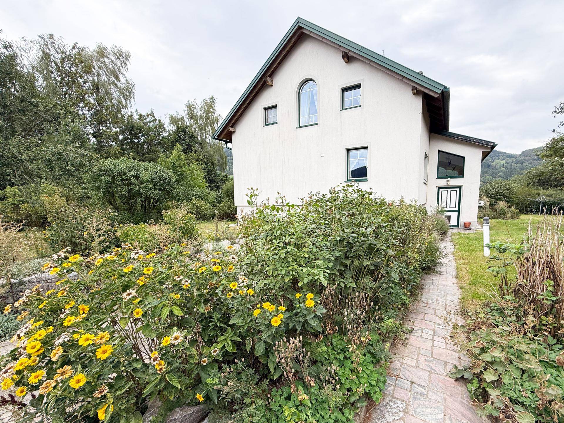 Charmantes Einfamilienhaus mit blühenden Blumenbeeten und einem gepflasterten Gartenweg.