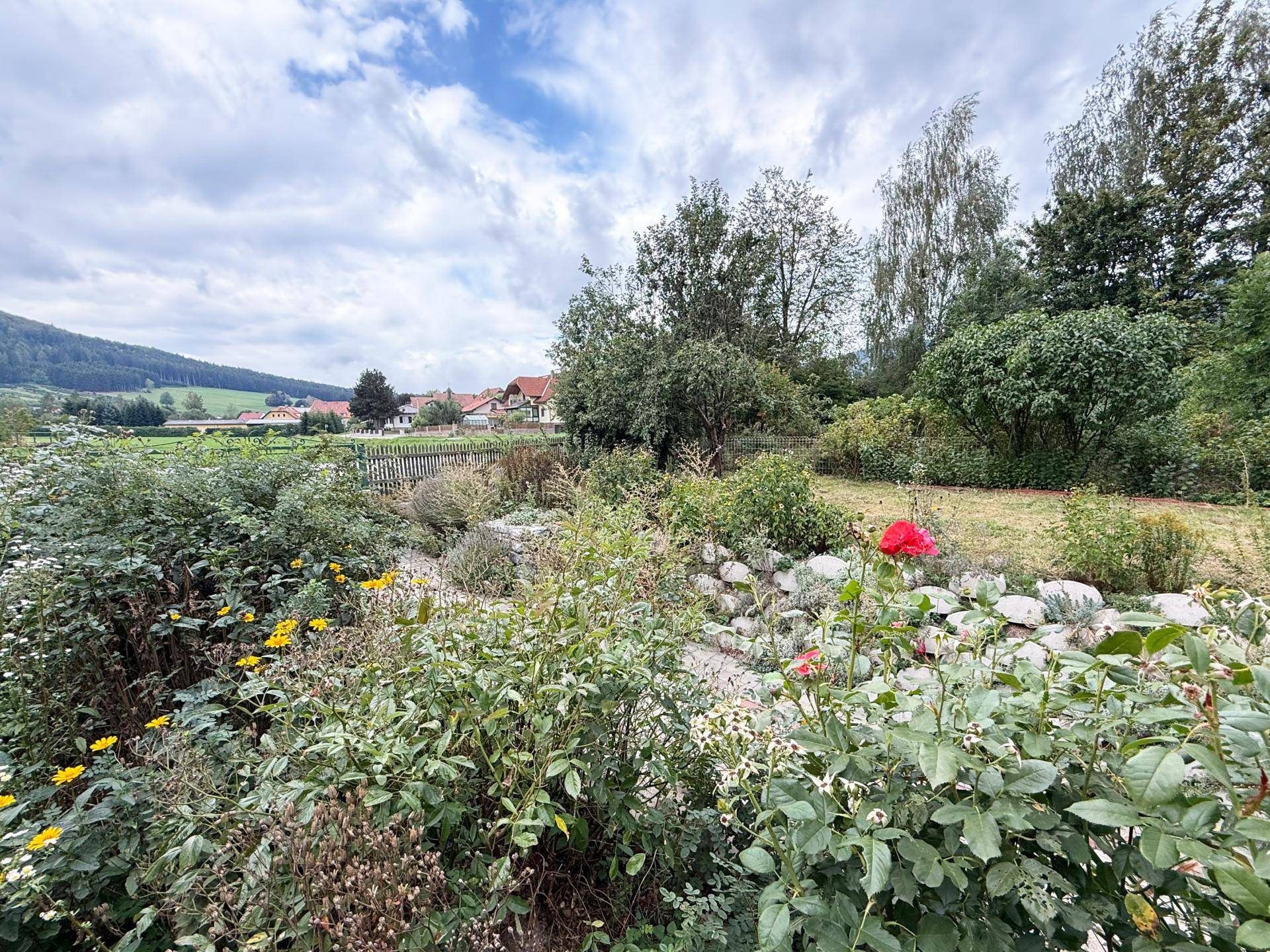 Blühender Garten mit Rosen und Blick auf ein malerisches Dorf und die umliegende Berglandschaft.