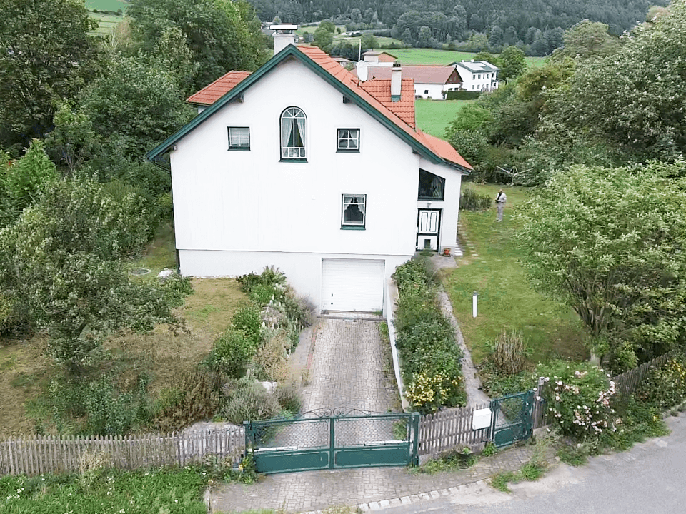 Luftaufnahme eines weißen Hauses mit grünem Dach, Garage und großem Gartenbereich.