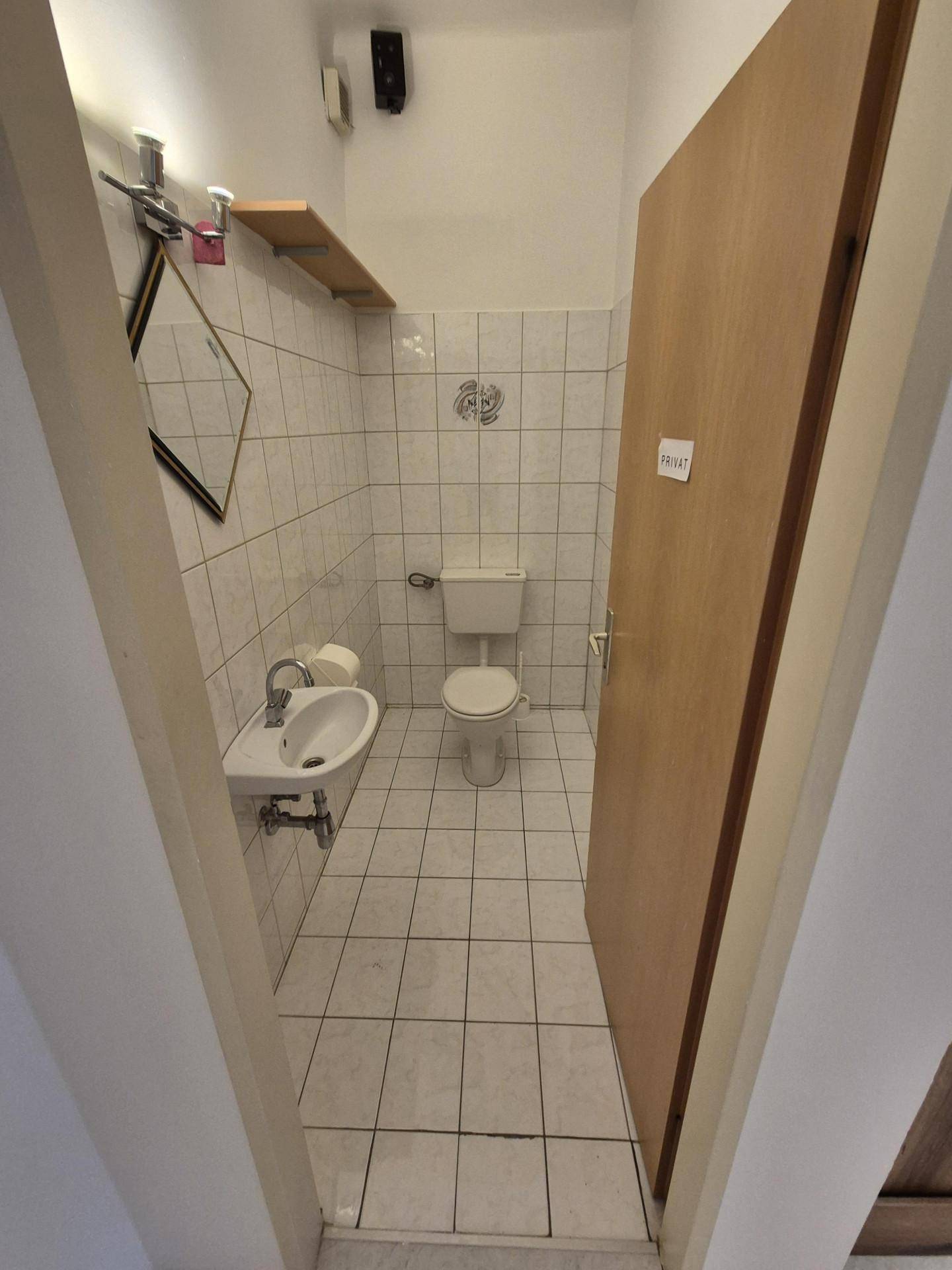 Einfaches Gäste-WC mit Toilette, Waschbecken und Spiegel, ausgestattet mit hellen Fliesen.