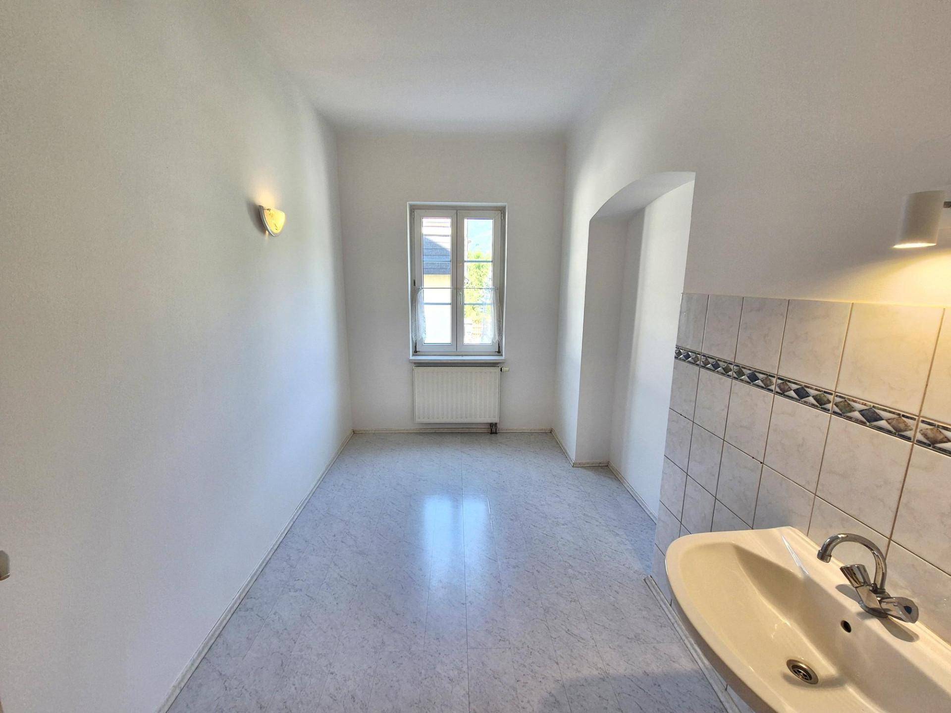 Heller Raum mit Waschbecken und Fenster, ausgestattet mit einfachem Bodenbelag und Wandfliesen.