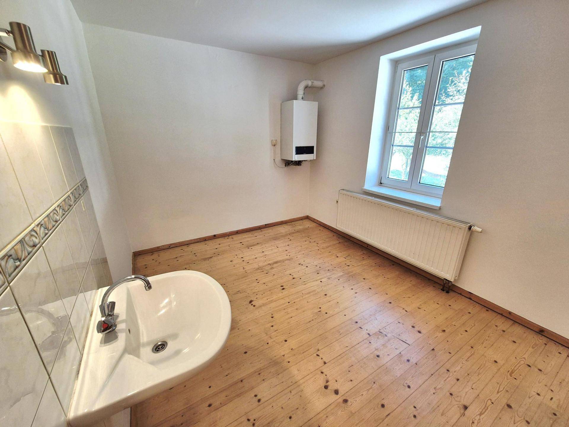 Praktischer Raum mit Holzdielenboden, Waschbecken und Fenster, inklusive Wandheizkessel.
