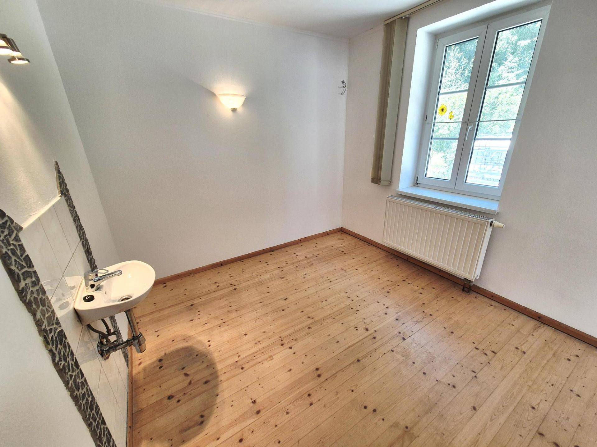 Heller Raum mit Holzdielenboden, Waschbecken und Fenster, geeignet für verschiedene Nutzungen.